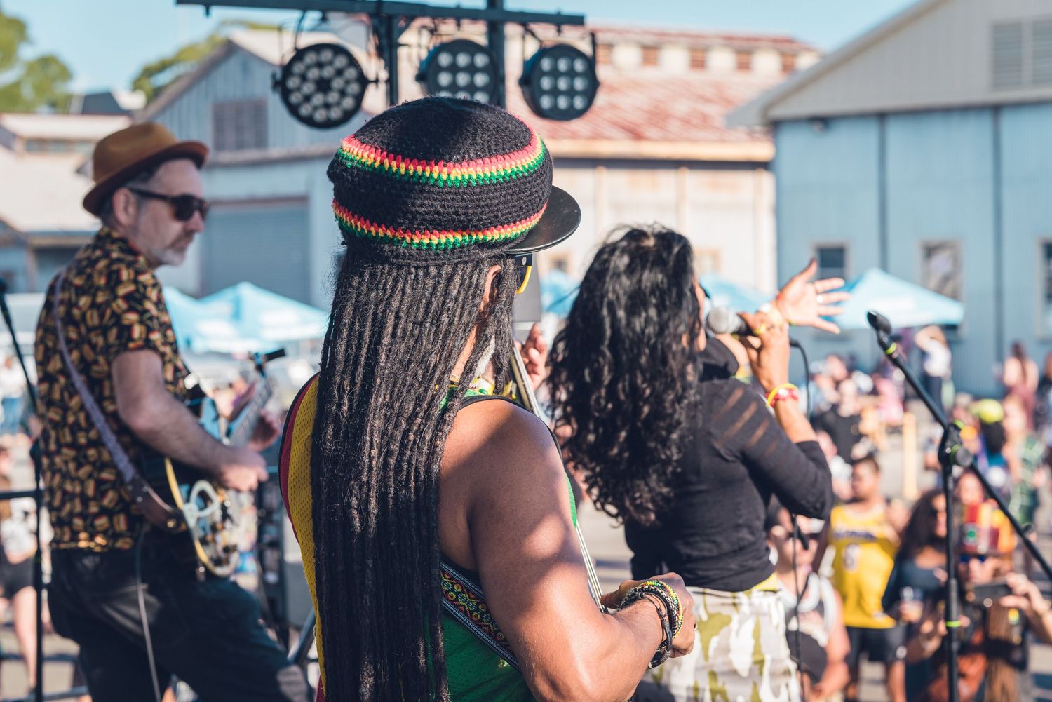 Reggae band performing outdoors with braided vocalist in green top and Rasta hat on stage.