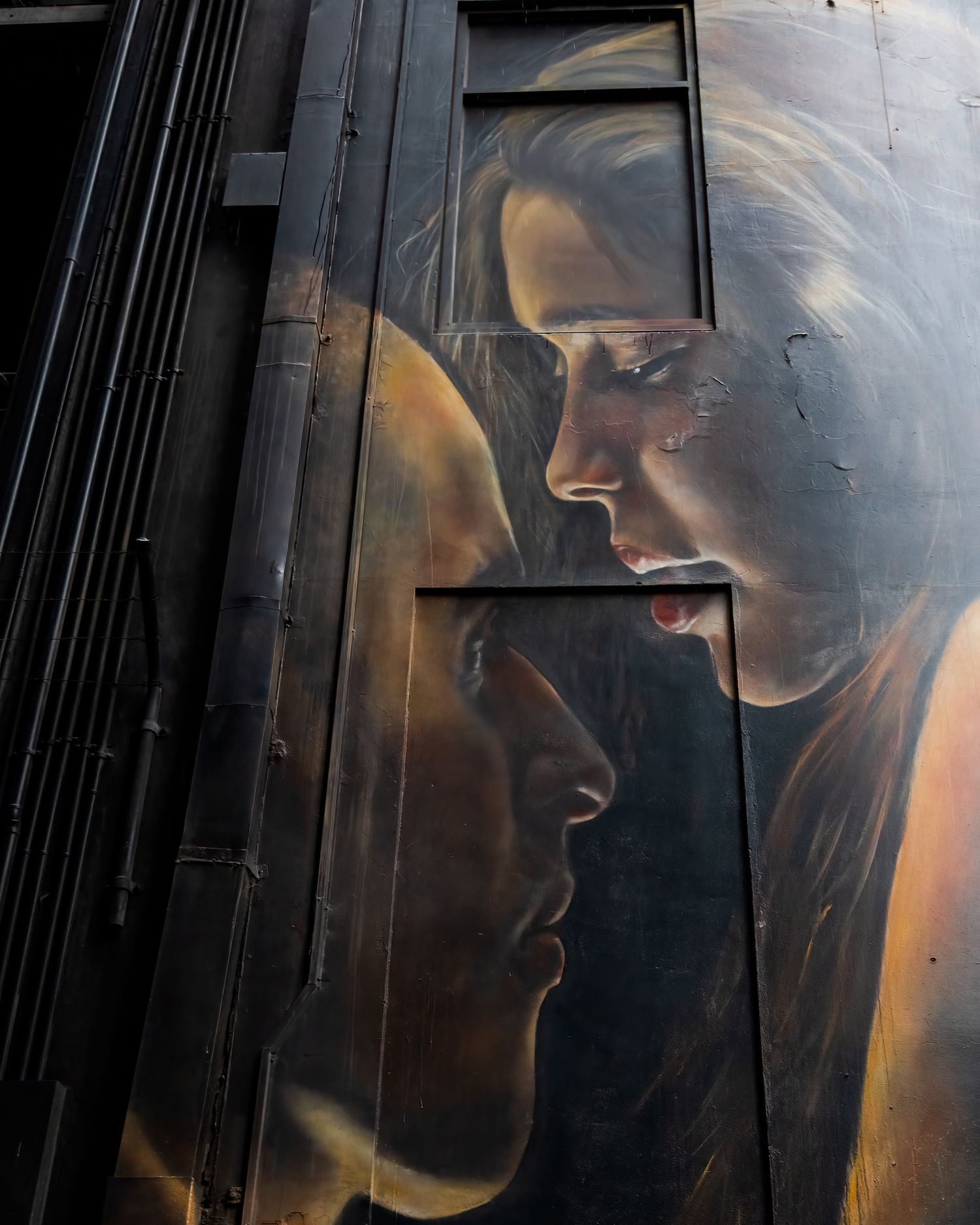 Large dramatic street art mural depicting two faces in profile painted on dark industrial metal panels.