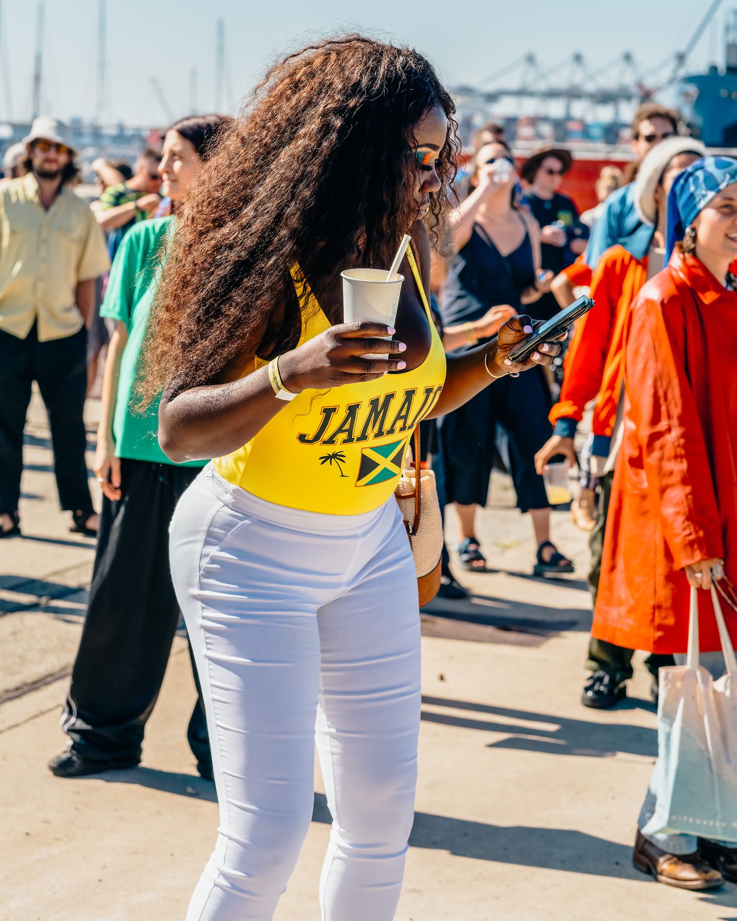Woman in Jamaica top and white jeans at outdoor music festival.