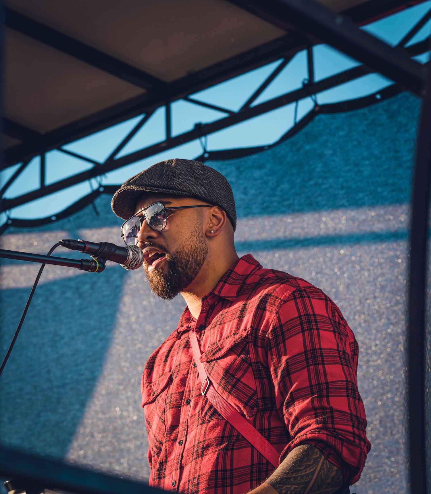 Male vocalist in red flannel shirt and cap singing at outdoor music festival.