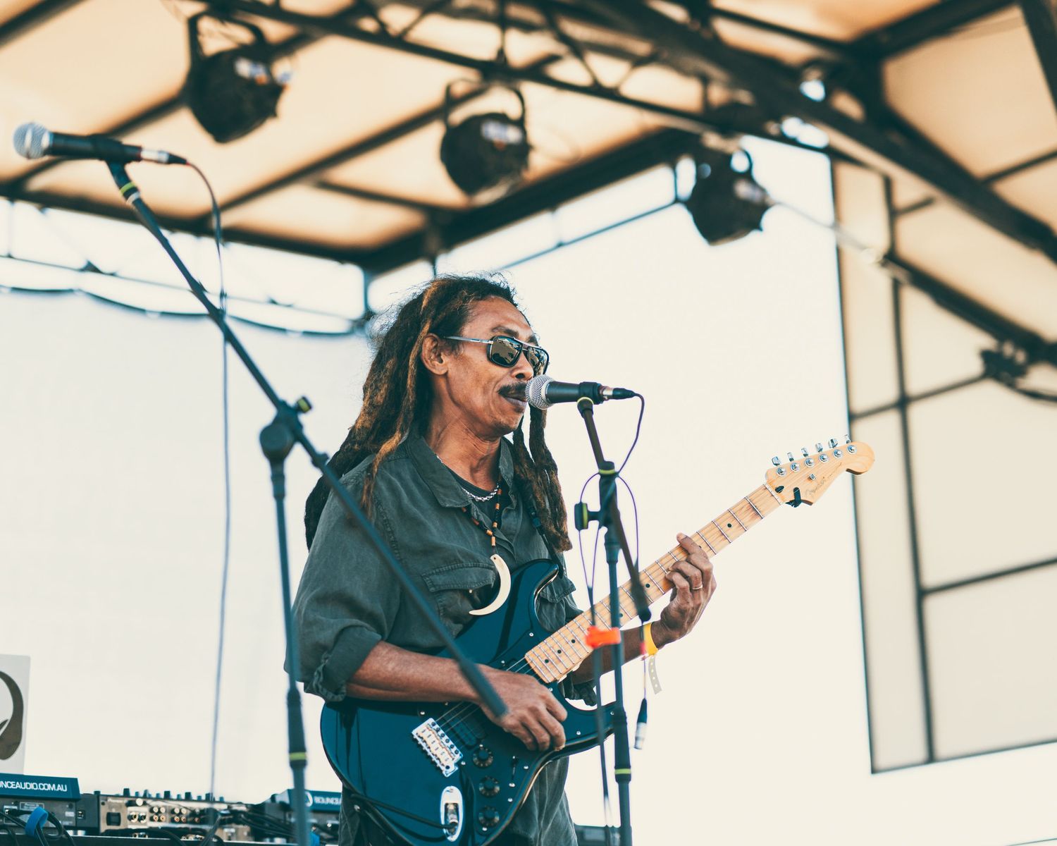 A dreadlocked guitarist with sunglasses performs on stage at the Jamaican Music and Food Fest outdoor event.