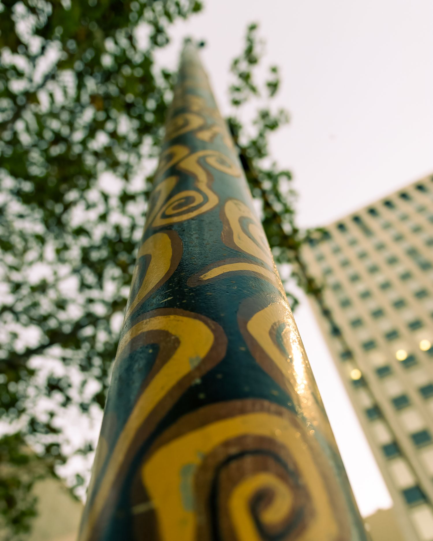 Close-up of a colorful painted pole with swirling yellow patterns against a blurred urban background.