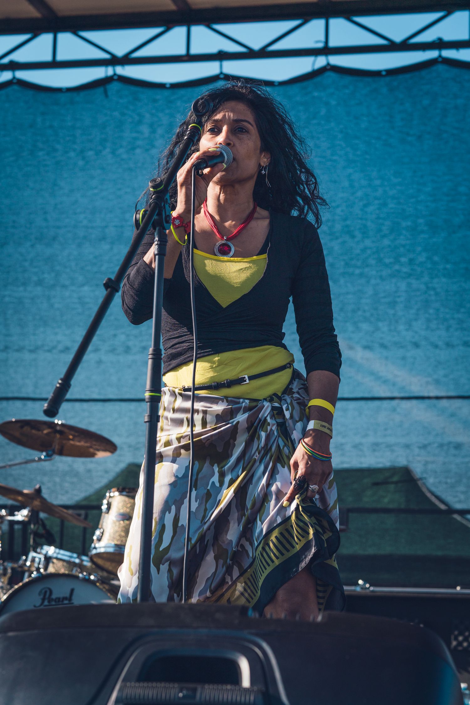 Female singer performing on outdoor stage in black top and patterned skirt at music festival.