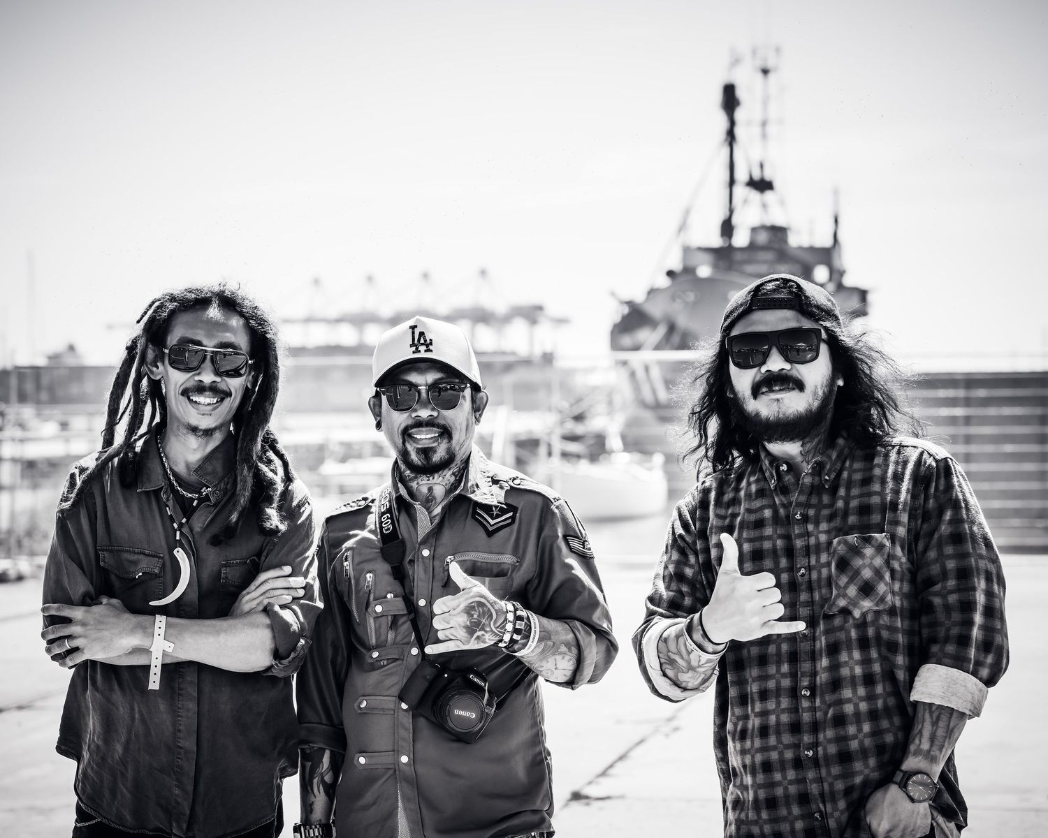 Three smiling men with dreadlocks posing at outdoor reggae festival.