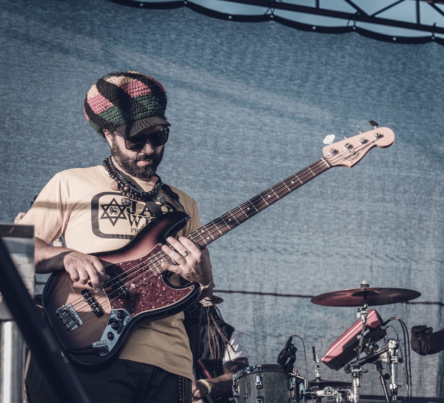 Reggae bassist wearing a rasta hat and Star of David necklace performing on stage with an electric bass guitar.