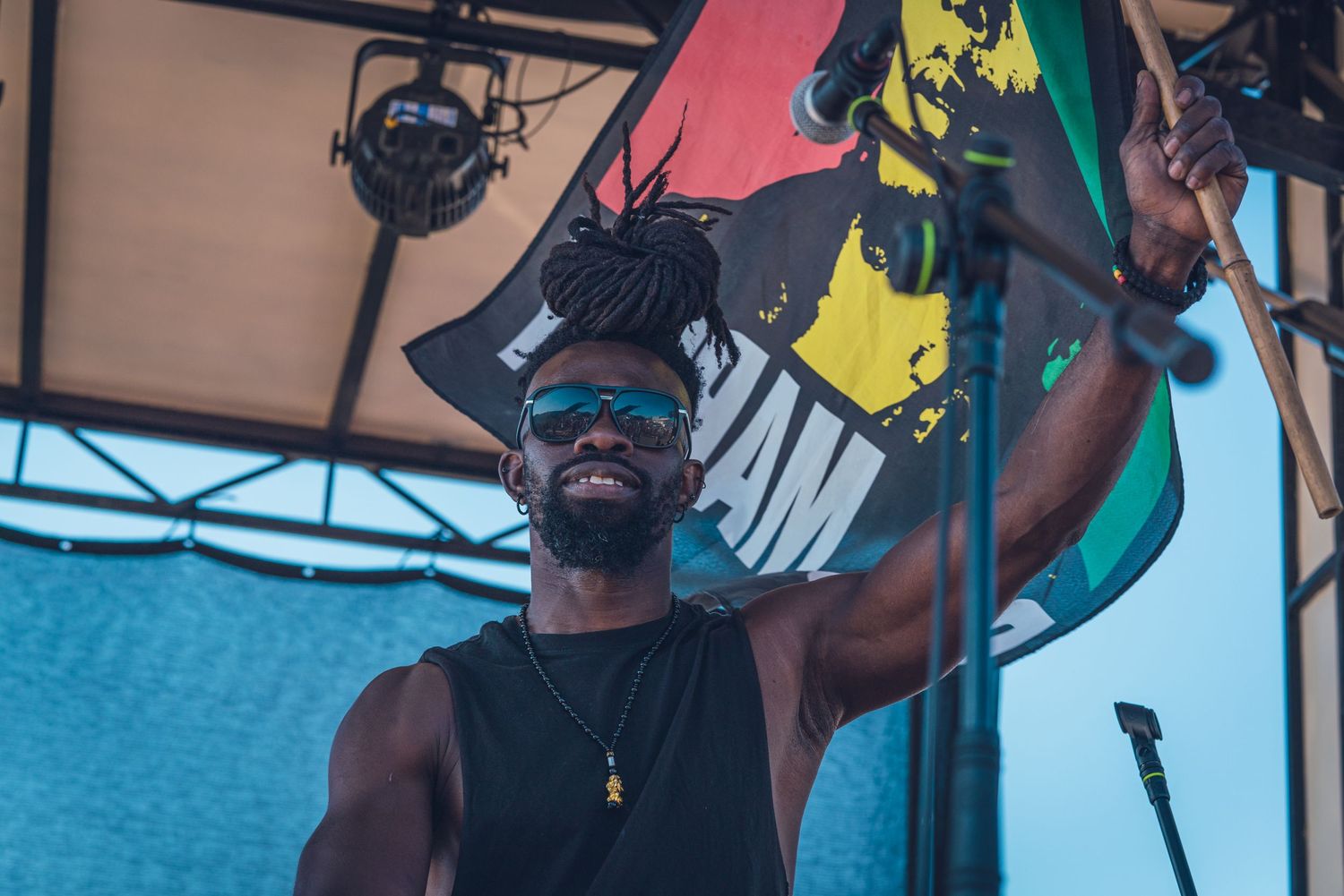 A smiling performer holds up a Bob Marley flag on stage at an outdoor Jamaican music festival.