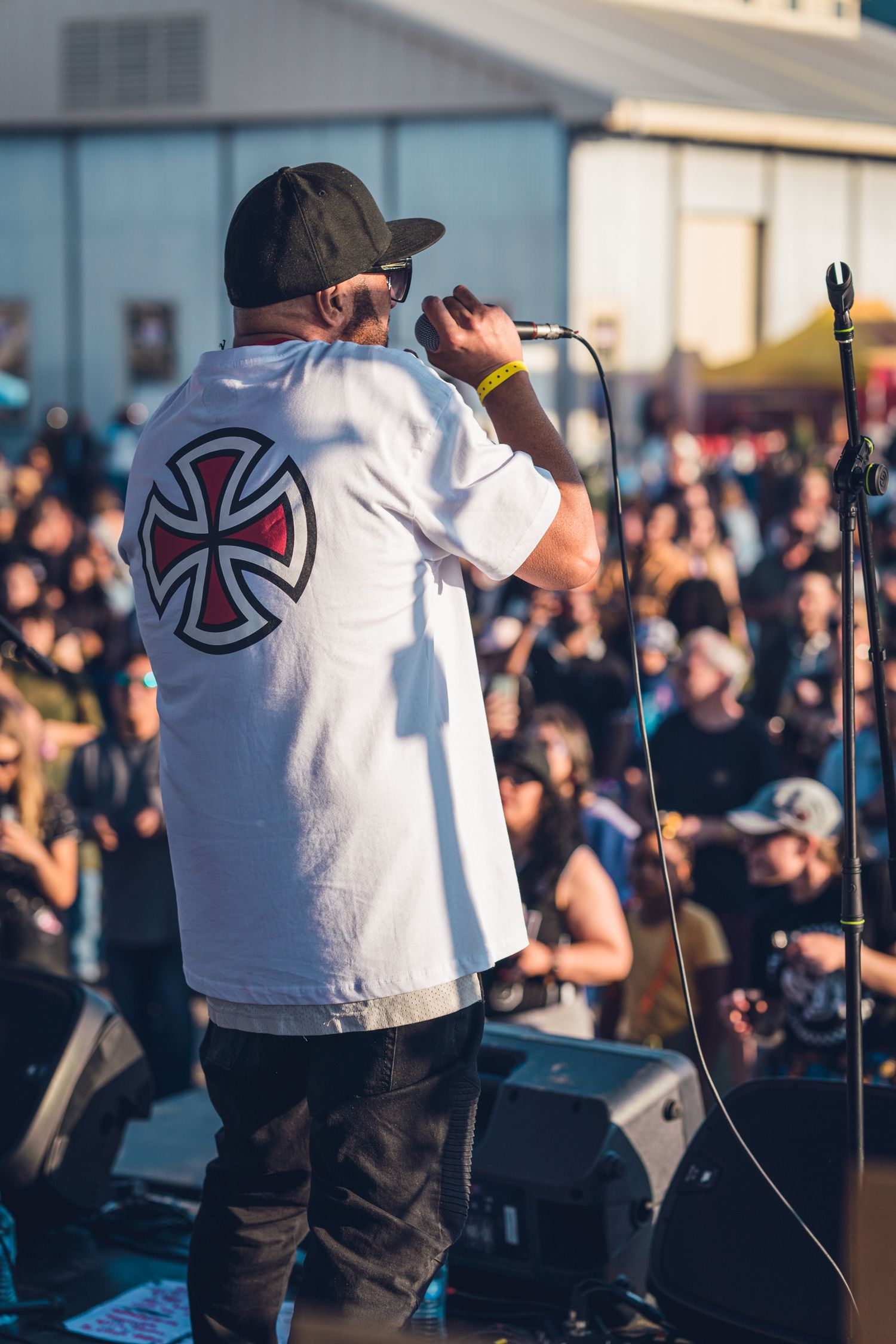 Performer in Independent truck t-shirt singing into microphone on stage before large crowd.