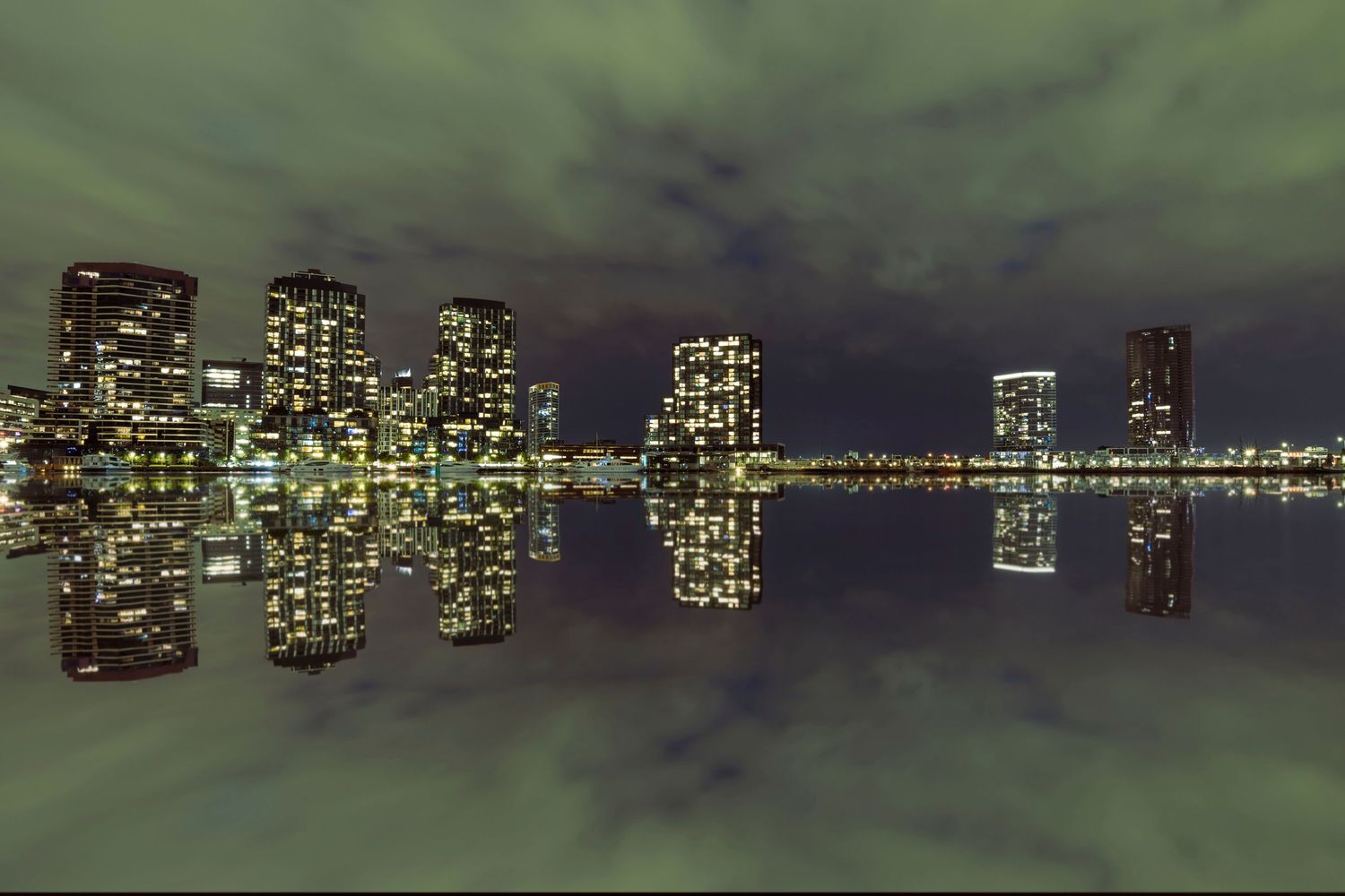 Symmetrical night cityscape of illuminated skyscrapers perfectly reflected in calm dark harbor waters.