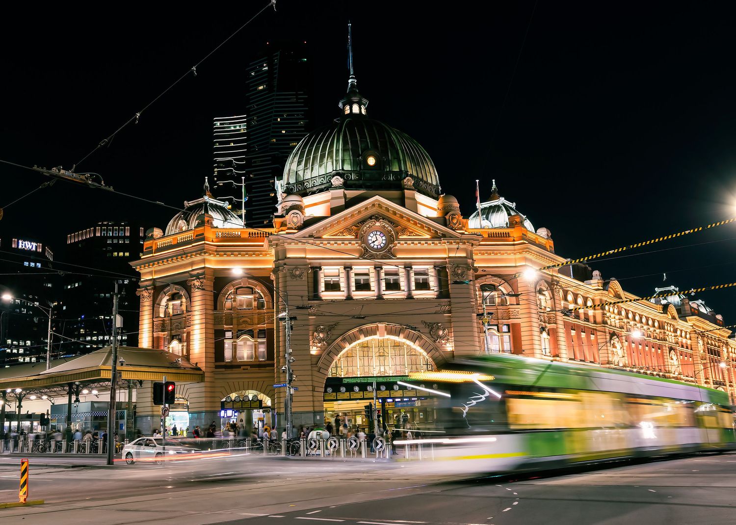 Flinders Street Station glowing at night with a green tram in motion blur captured in long exposure.