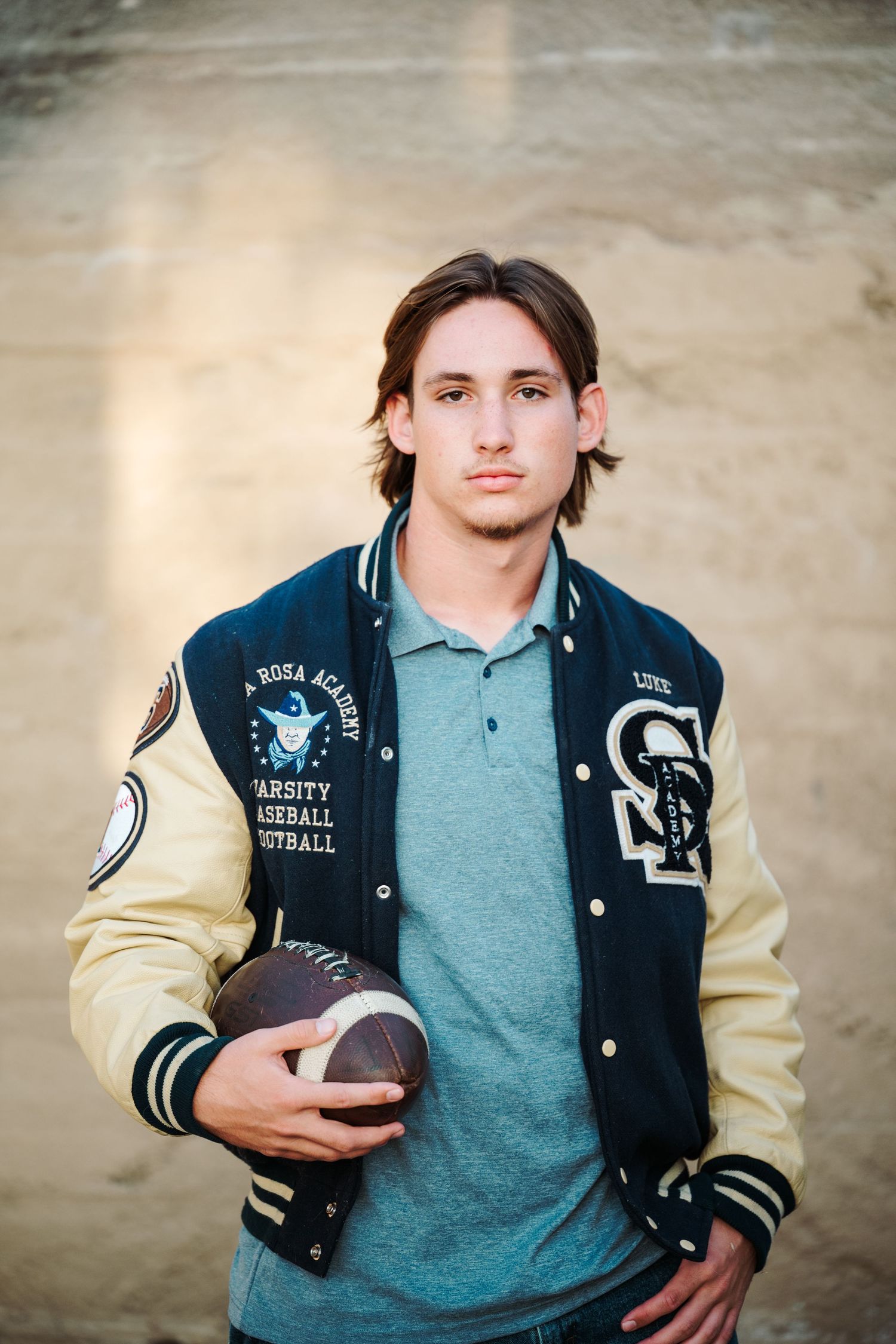 Young man holds football wearing Santa Rosa Academy varsity baseball football letterman jacket.