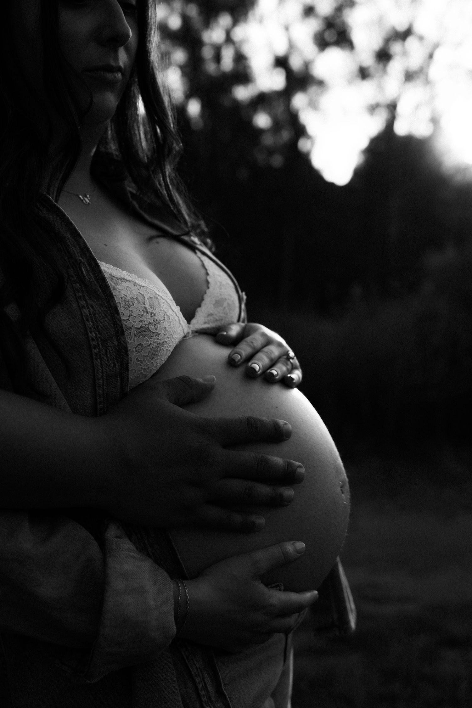 Black and white maternity photo of pregnant woman cradling bare baby bump outdoors.