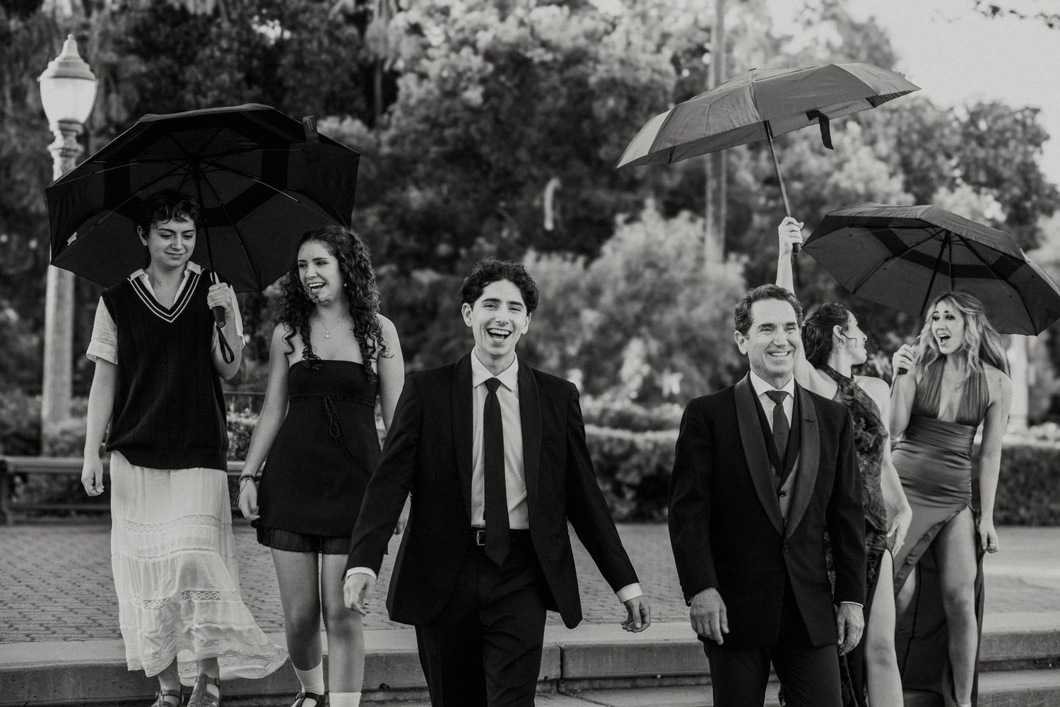 Black and white photo of elegantly dressed group walking with umbrellas on a rainy day.