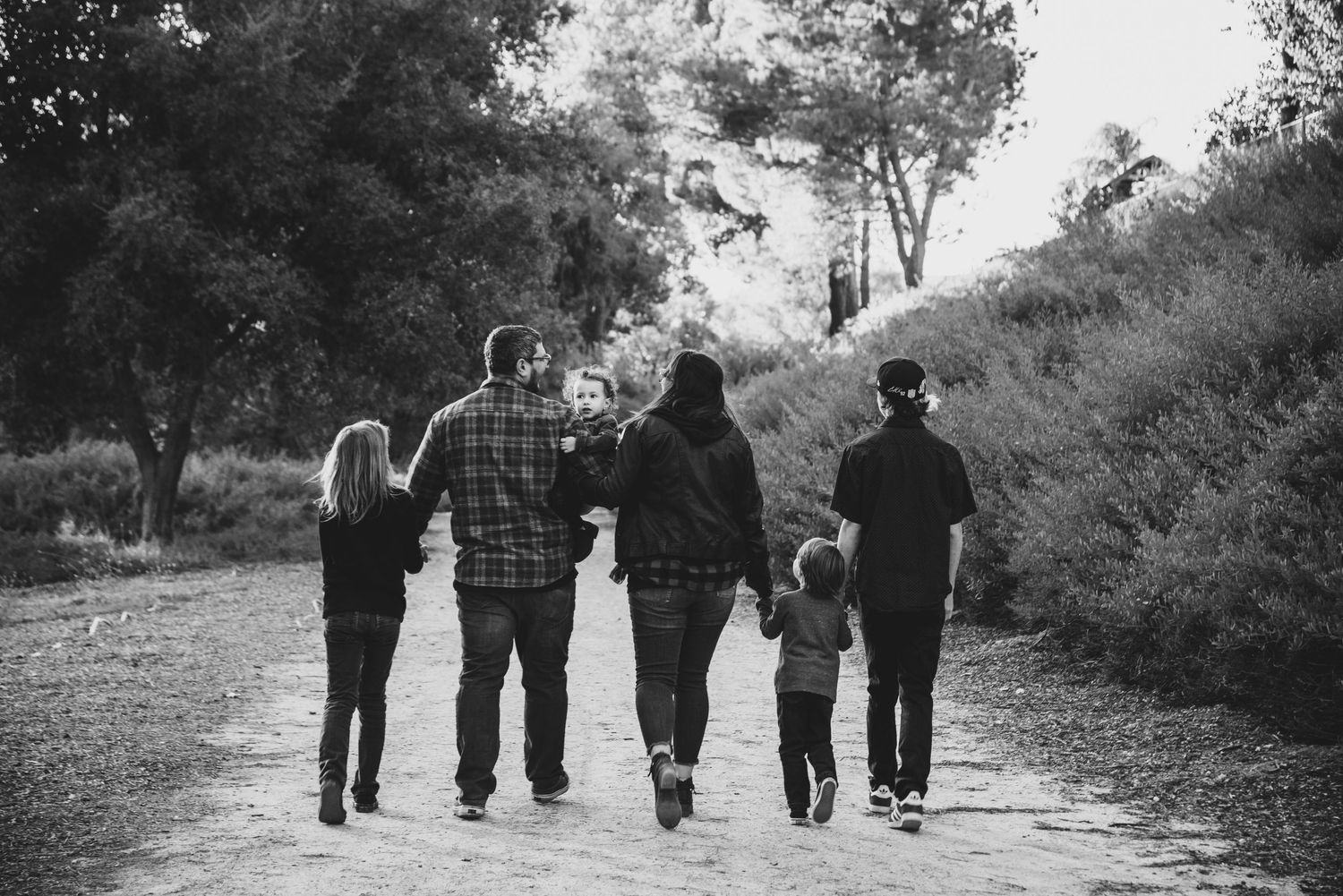 A family of six walks together down a scenic path surrounded by lush greenery in a black and white photo.