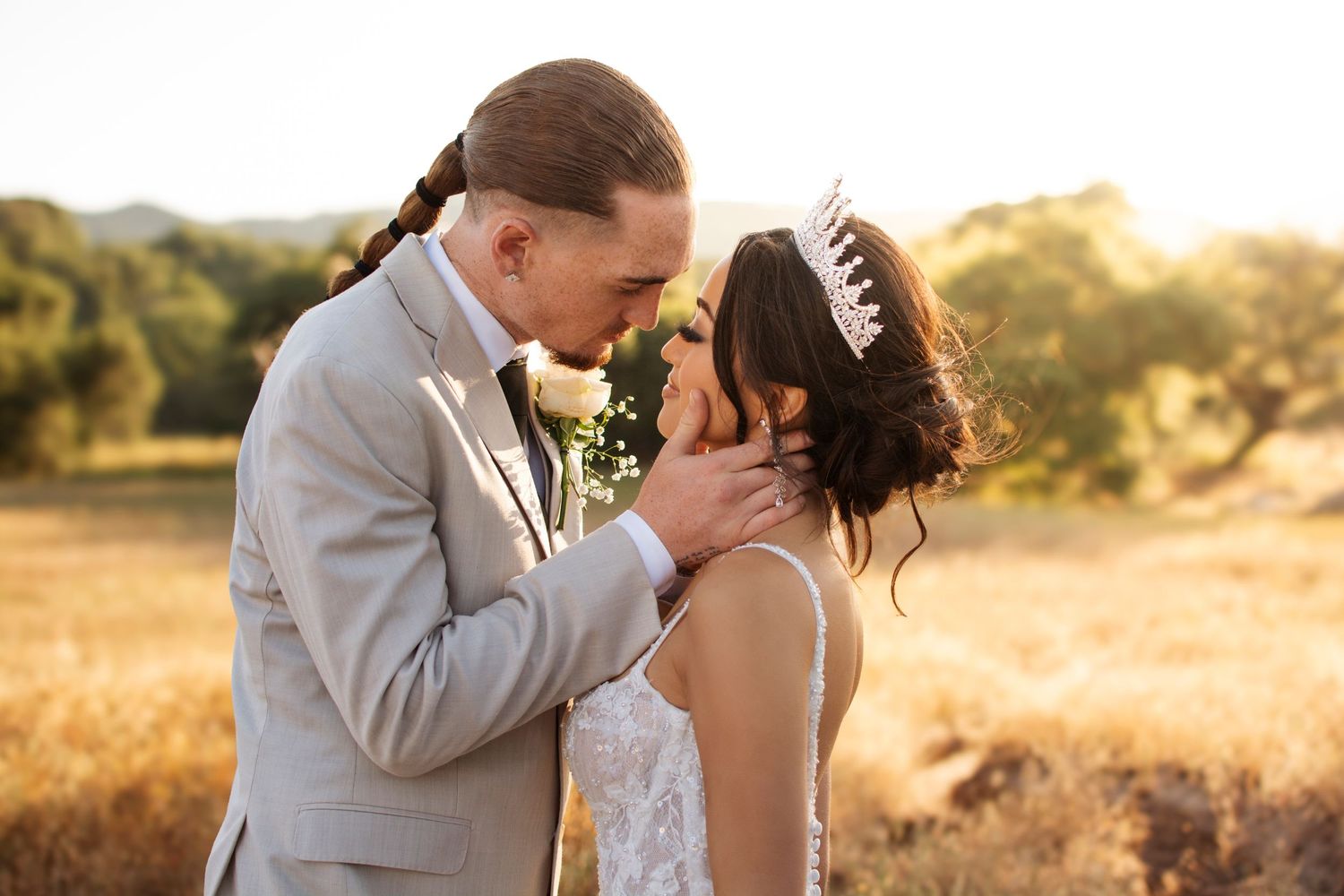 Groom tenderly holds bride's face during golden hour wedding portrait in a sunlit field.