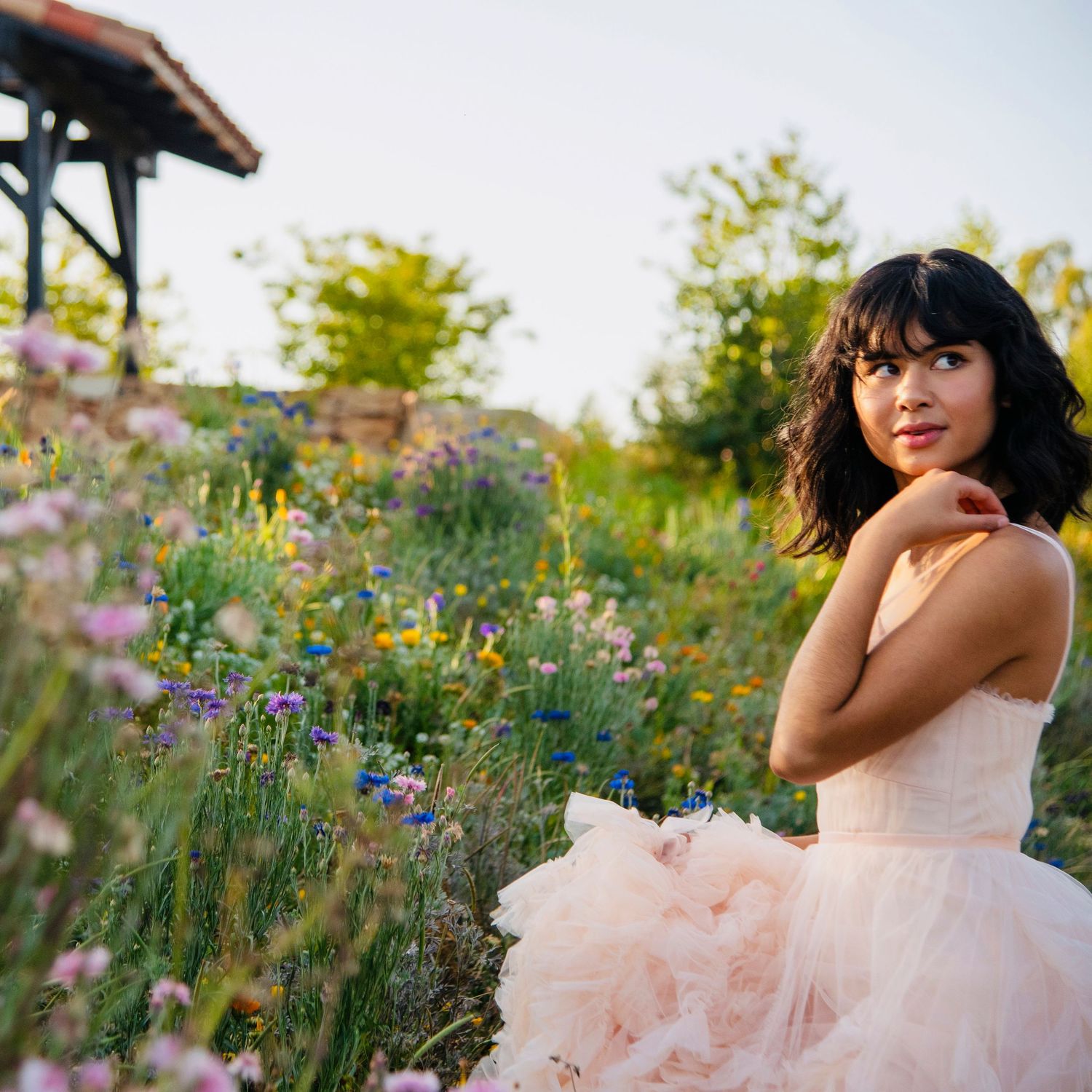 Young woman in pink tulle dress sitting in a colorful wildflower meadow at golden hour.
