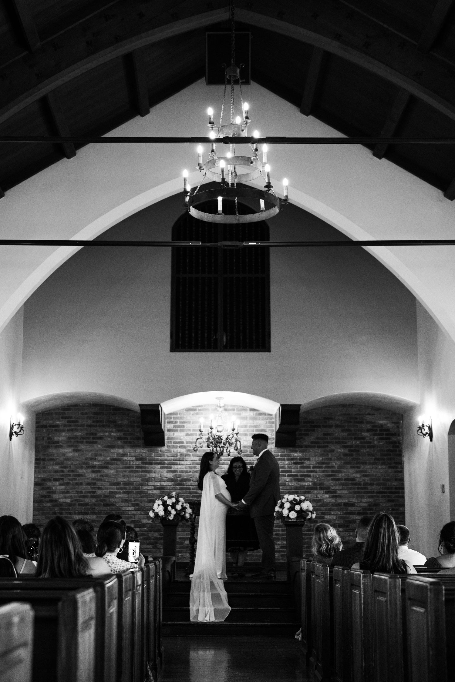 Black and white wedding ceremony photo of couple at the altar in a candlelit chapel.