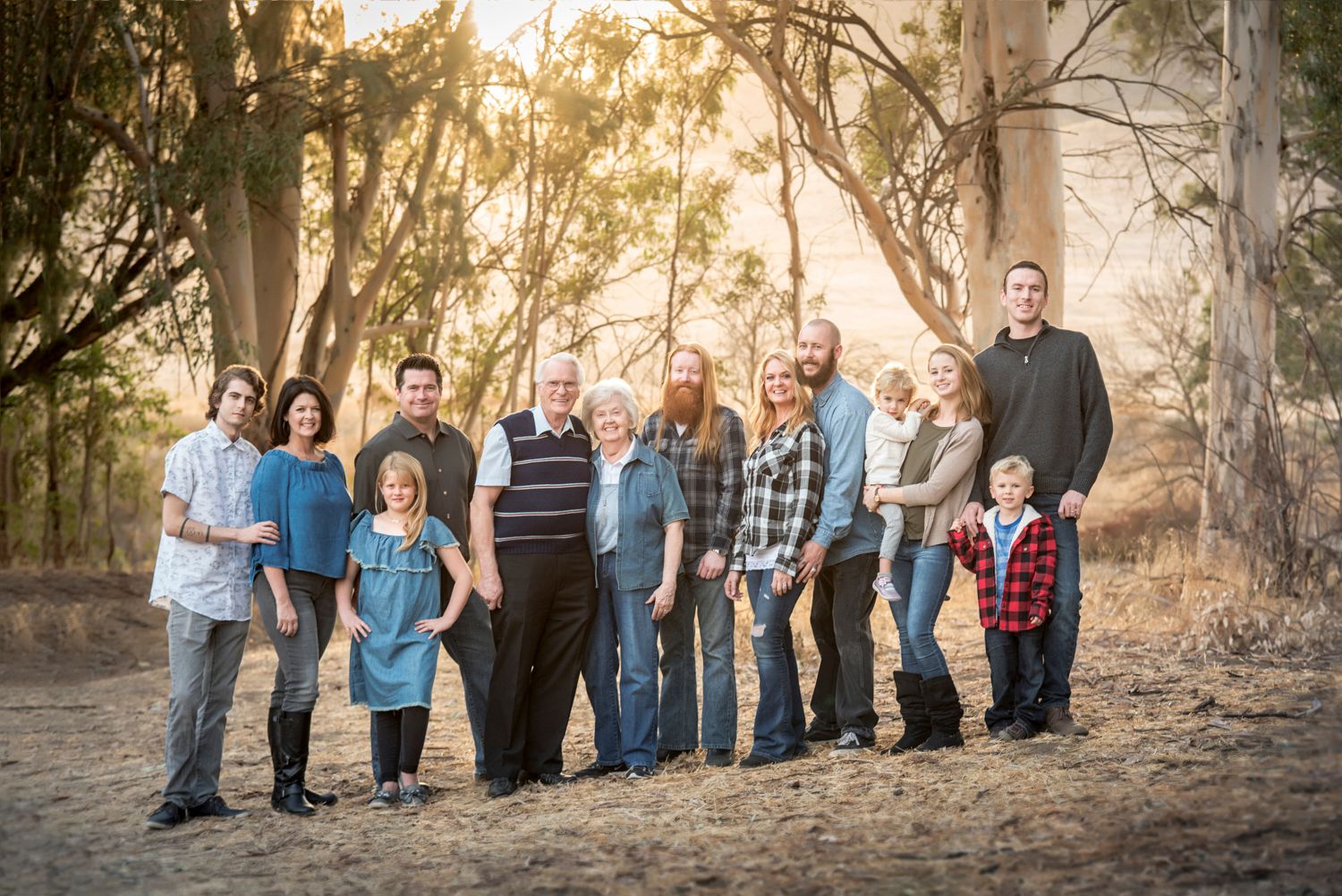 Large extended family posing together outdoors at golden hour among trees.