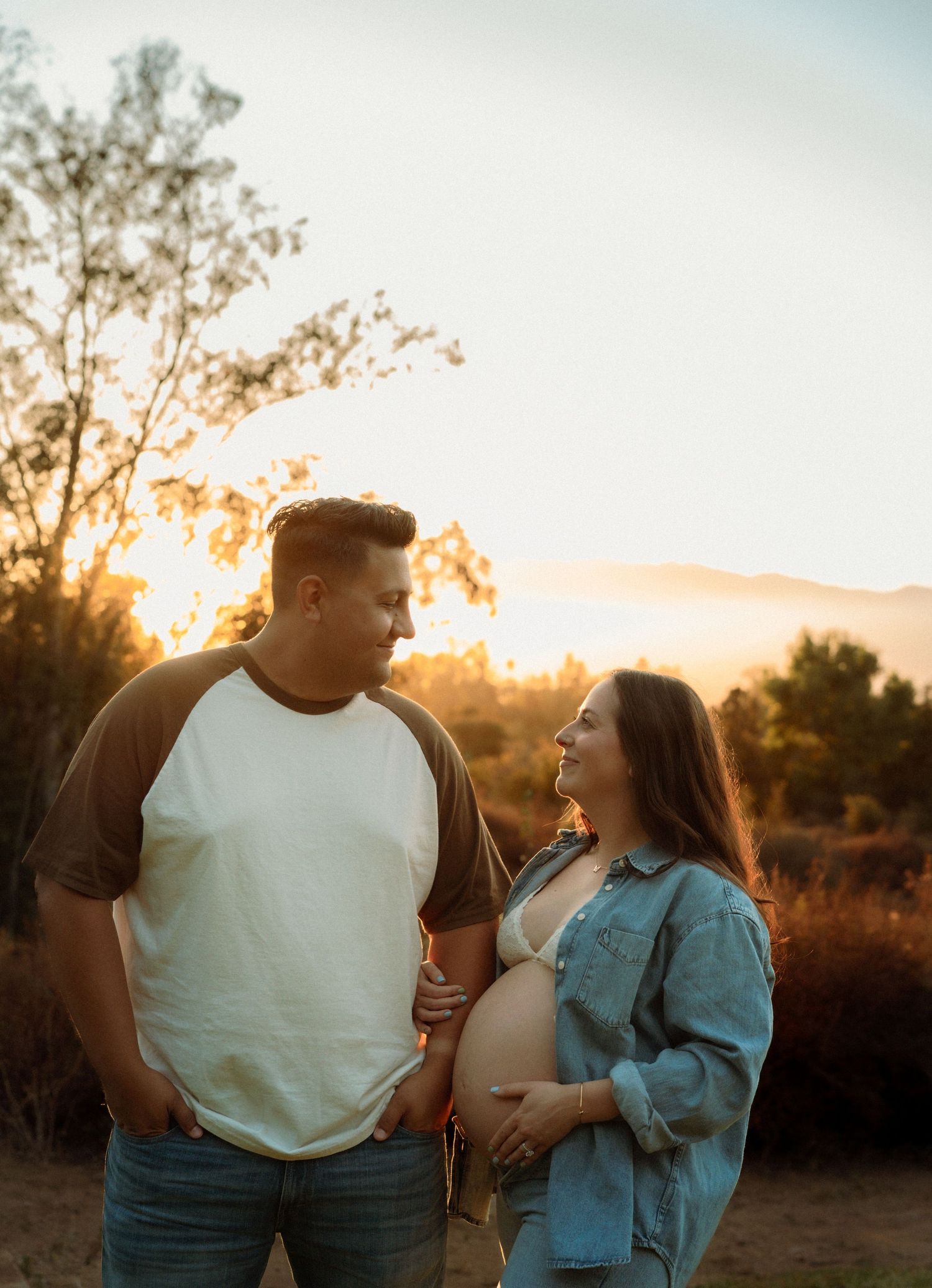 Expecting couple smiling at each other during golden hour maternity shoot outdoors.