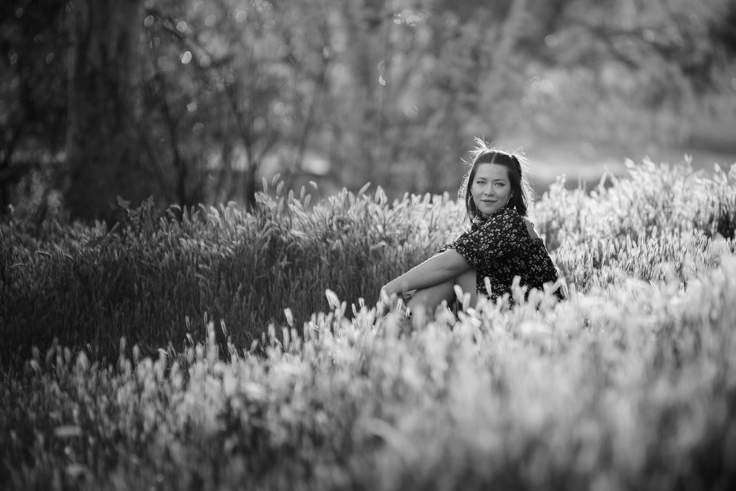 Black and white portrait of a young girl sitting peacefully in a field of tall wildflowers.