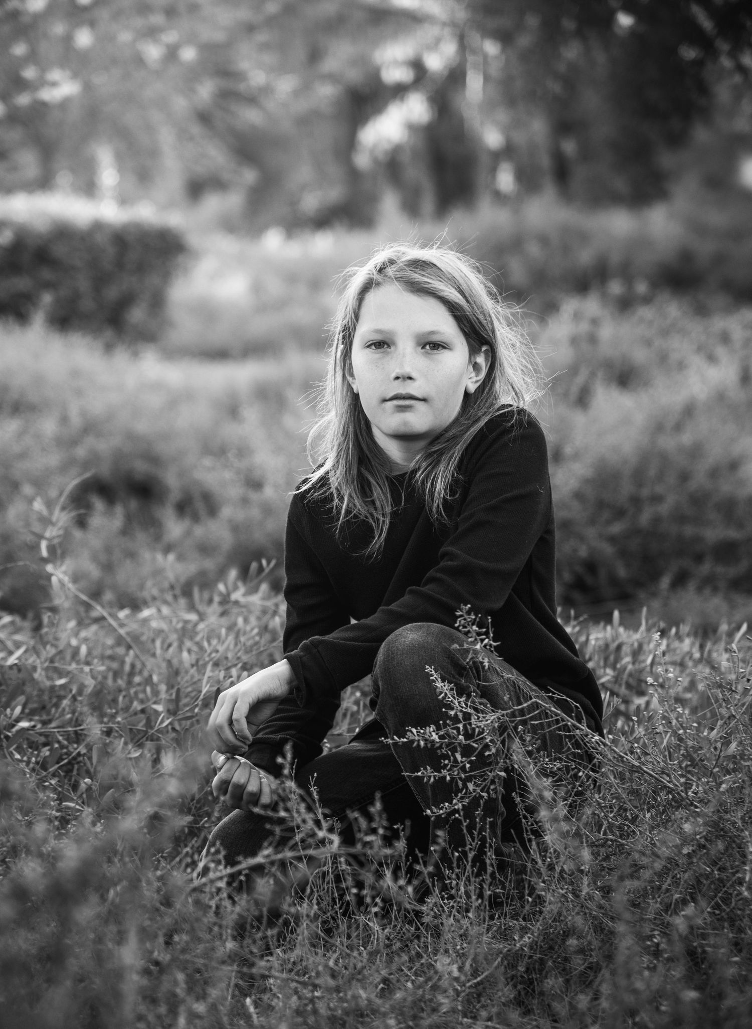 Young girl with long hair sitting in grass in black and white portrait.
