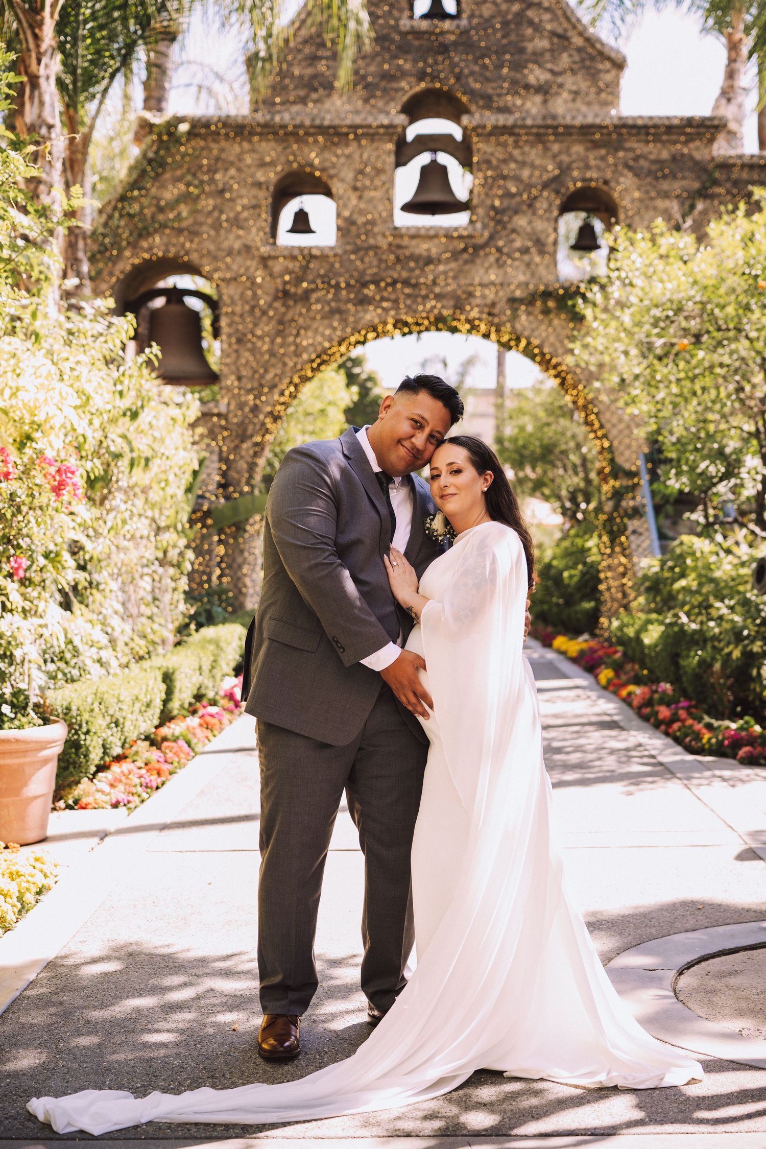 Bride and groom posing in front of a floral bell tower arch at a garden venue.