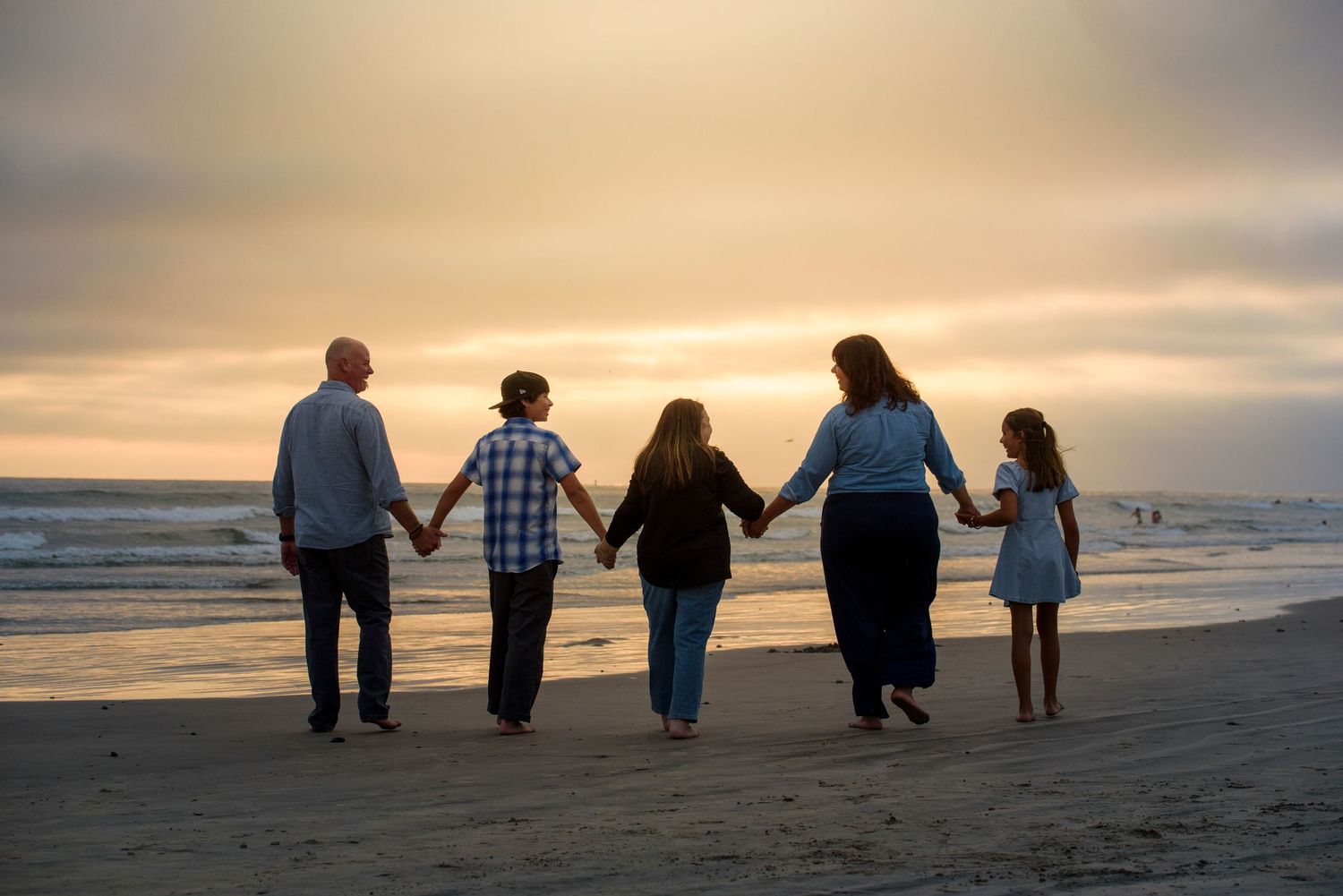 Family of five holding hands walking toward sunset on beach.