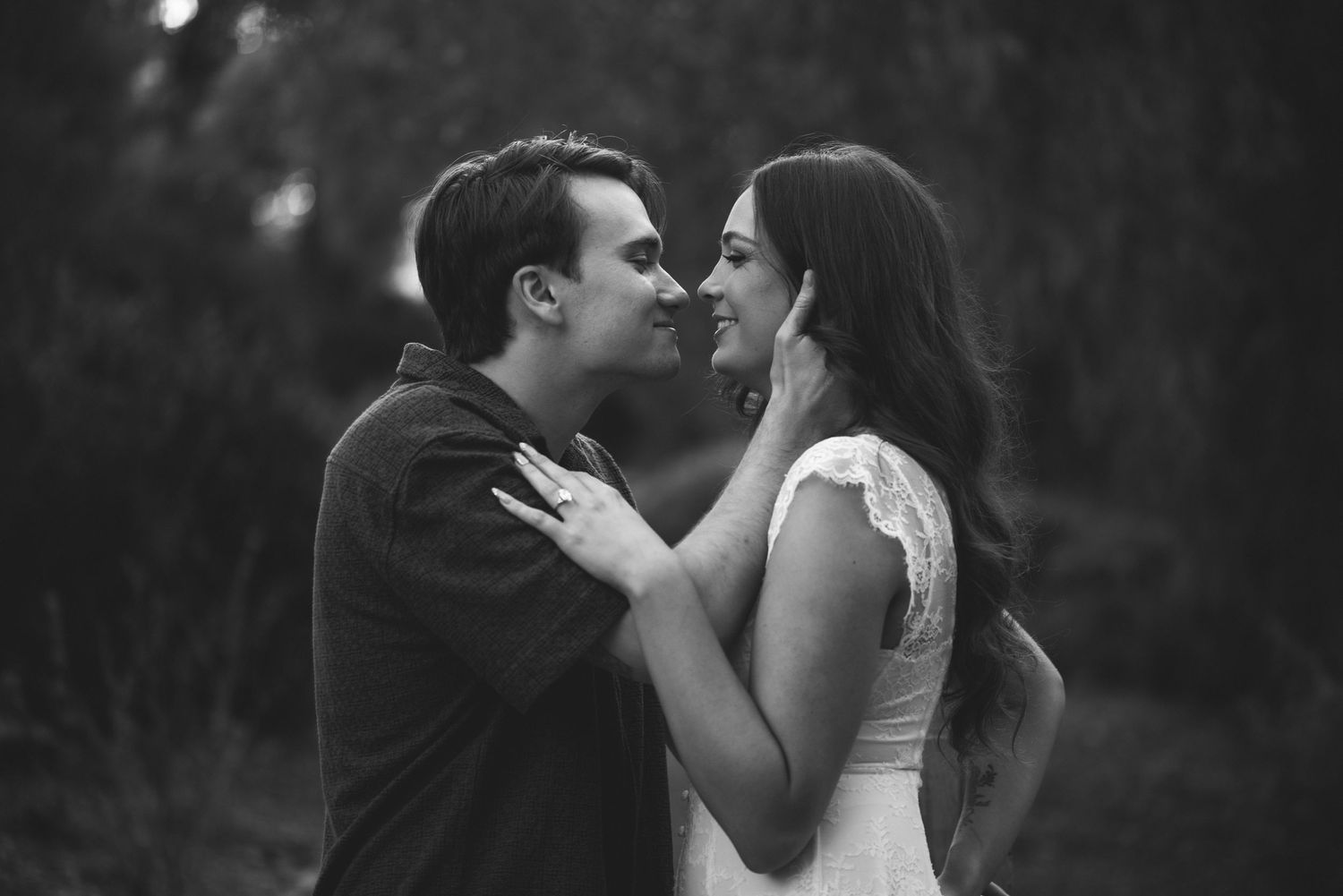Black and white photo of a romantic couple sharing an intimate moment outdoors, nearly kissing in soft natural light.