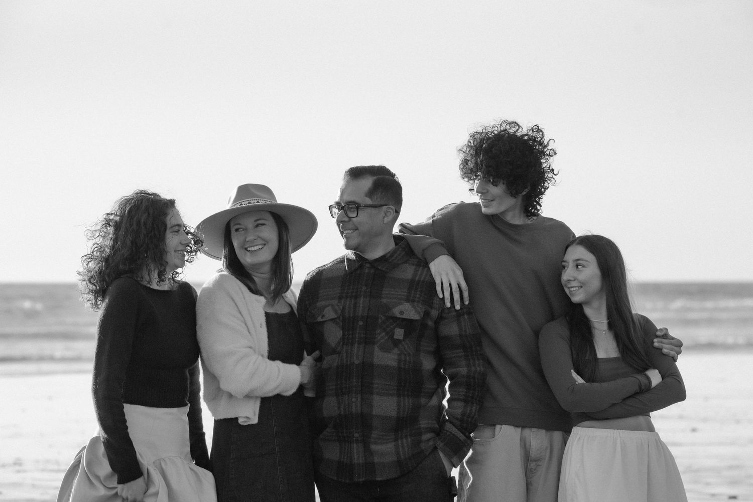 A family of five smiles together on a beach in a black and white portrait photo.