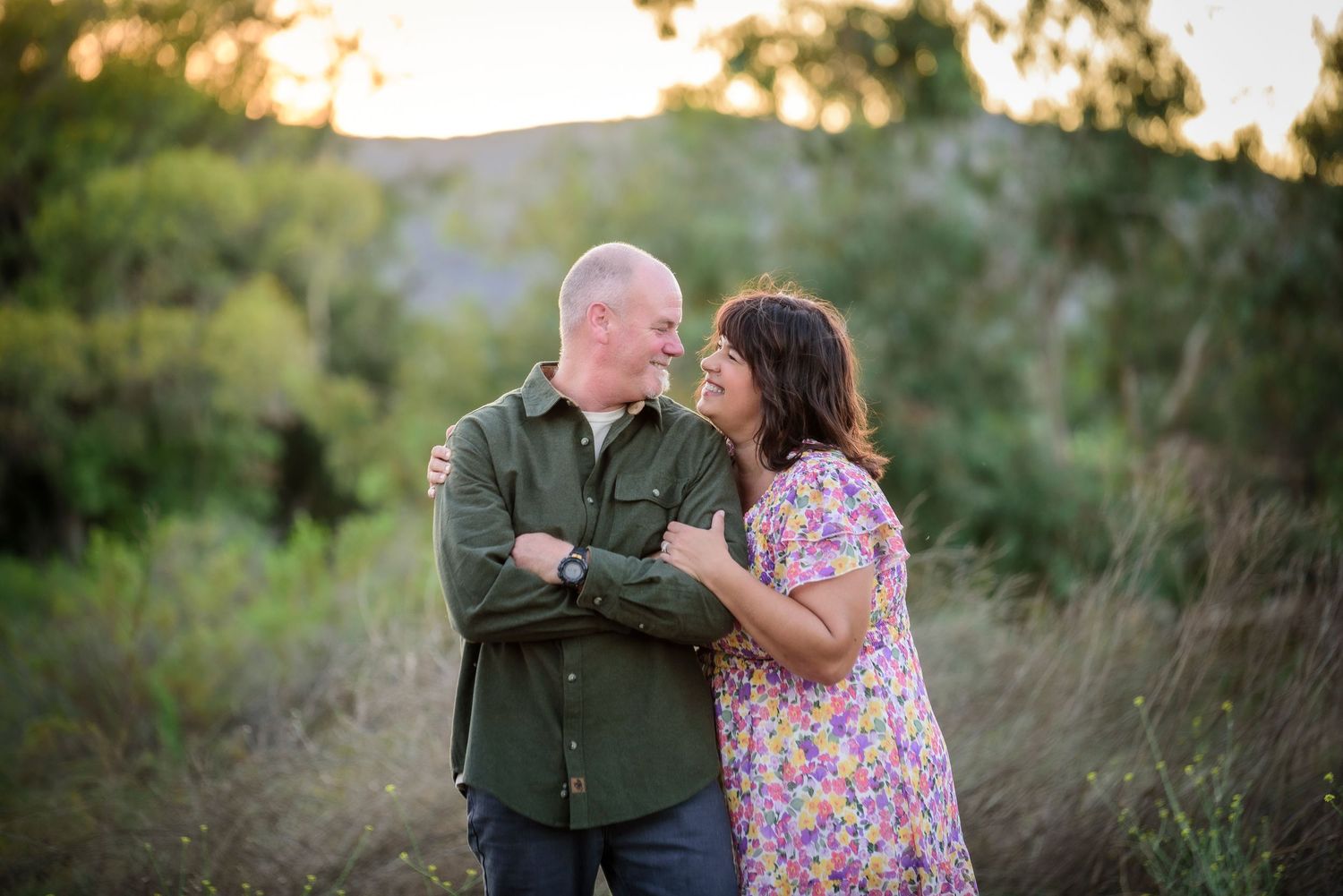 Happy couple smiling at each other in a sunlit outdoor field setting.