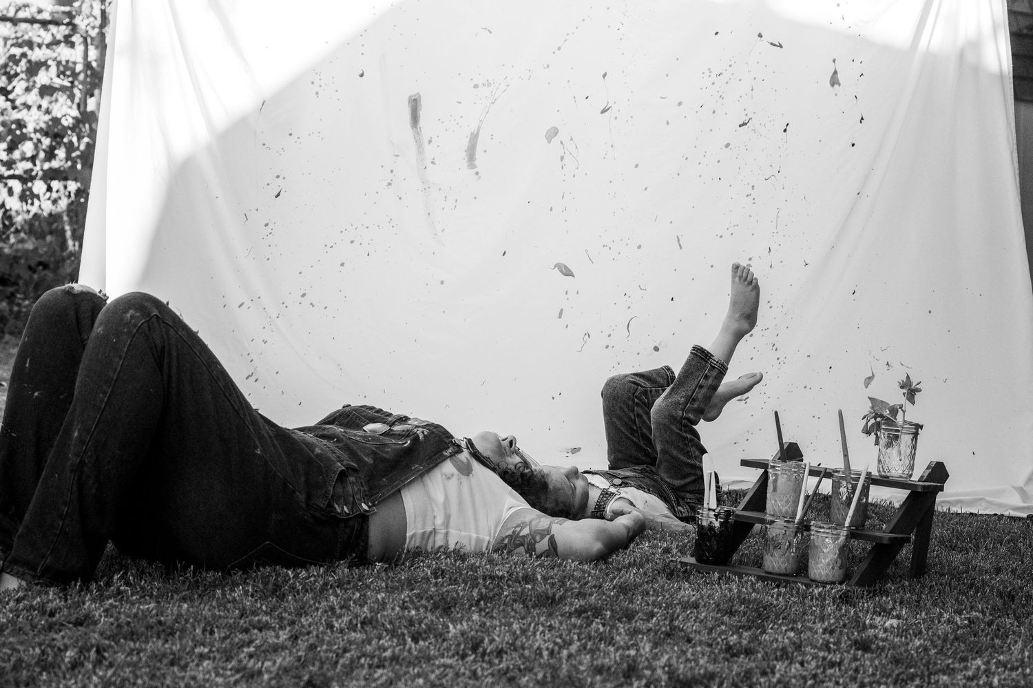 Black and white photo of couple lying on grass under white sheet, playfully kicking their feet.
