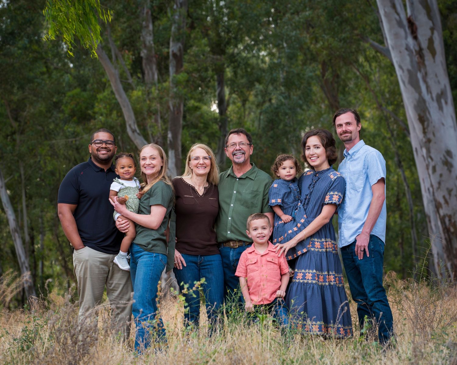 Extended family of eight smiling together in a lush green meadow.