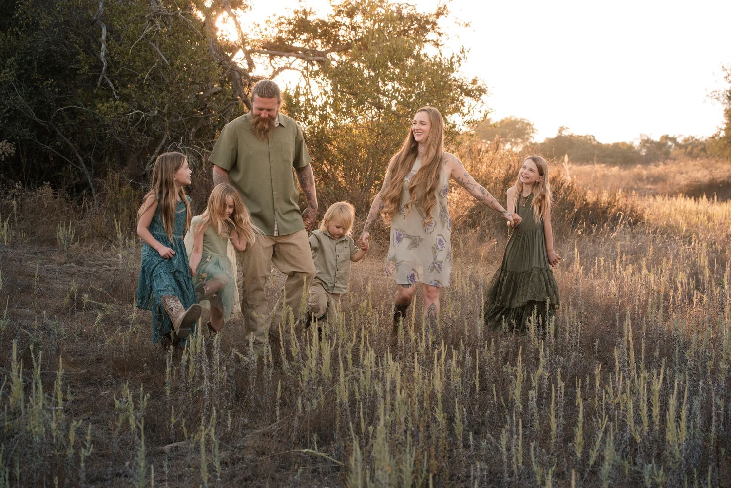 Happy family of six walking through a golden field at sunset, holding hands and laughing.
