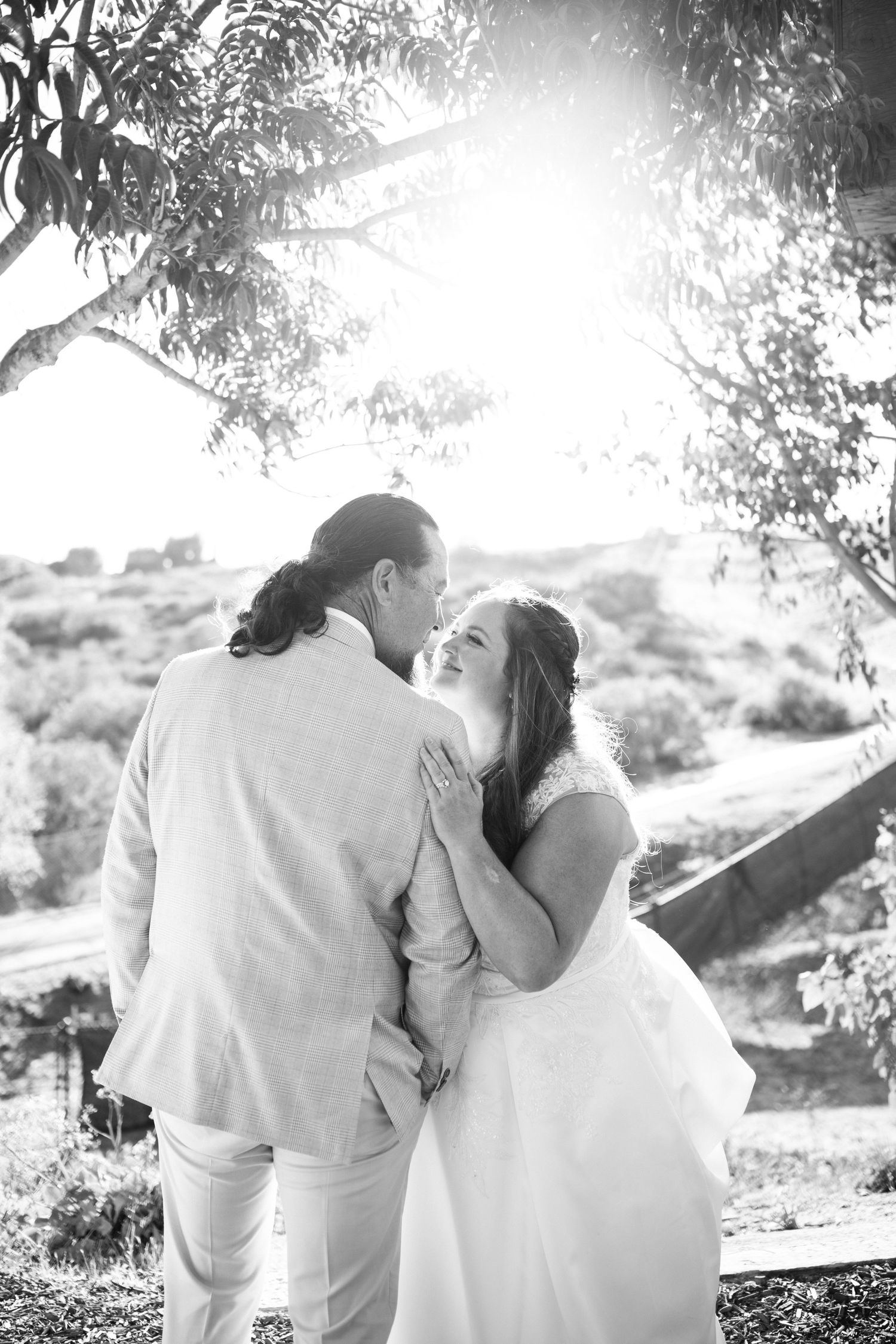 Black and white photo of bride and groom sharing an intimate moment under a tree in outdoor setting.