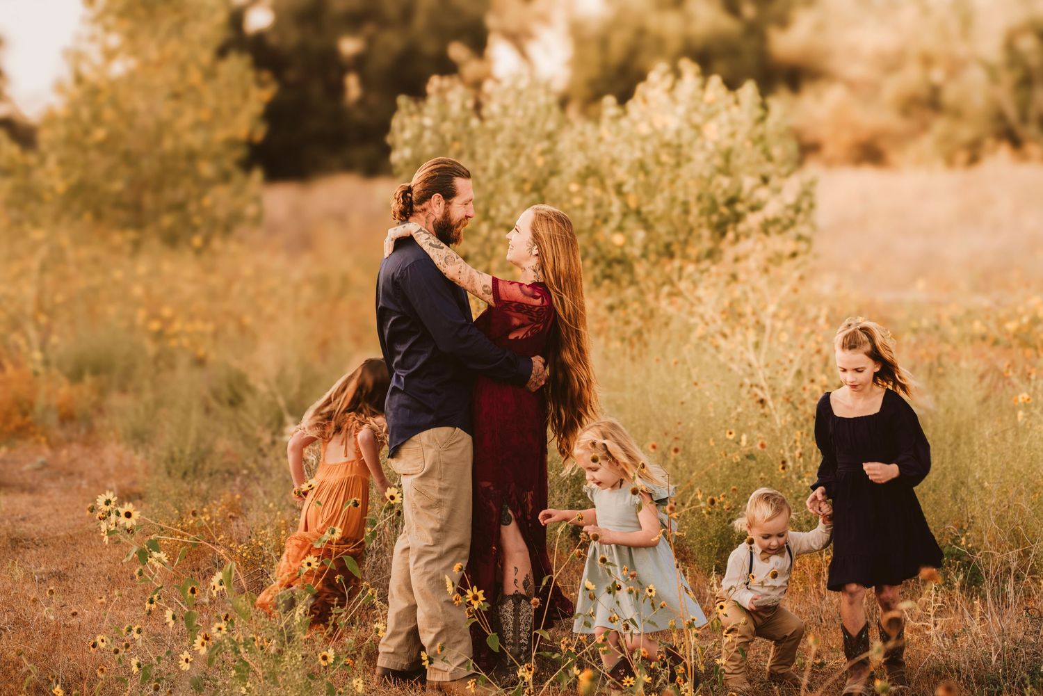 A family with young children embraces in a sunlit wildflower field at golden hour.