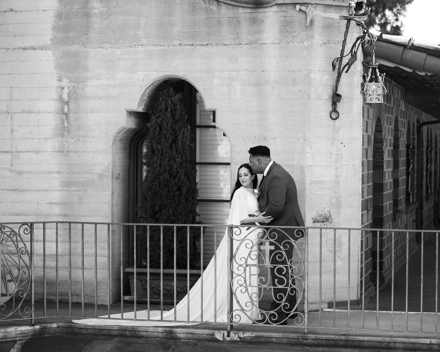 Black and white photo of newlyweds sharing a kiss on an ornate iron balcony.