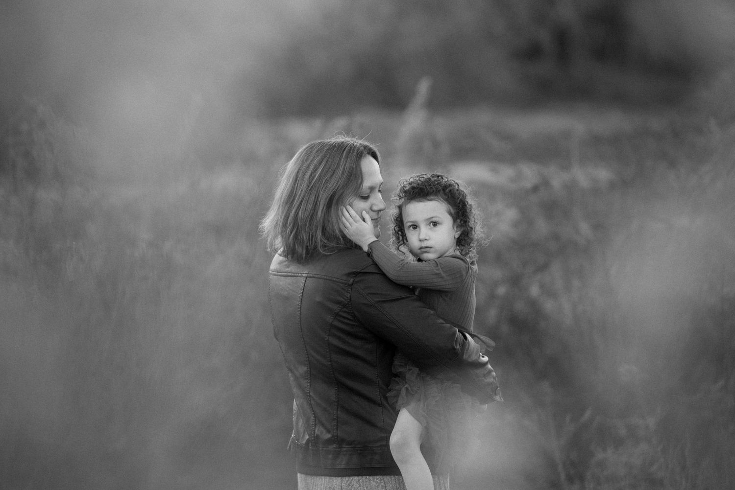 Mother tenderly holding young child in black and white field portrait.