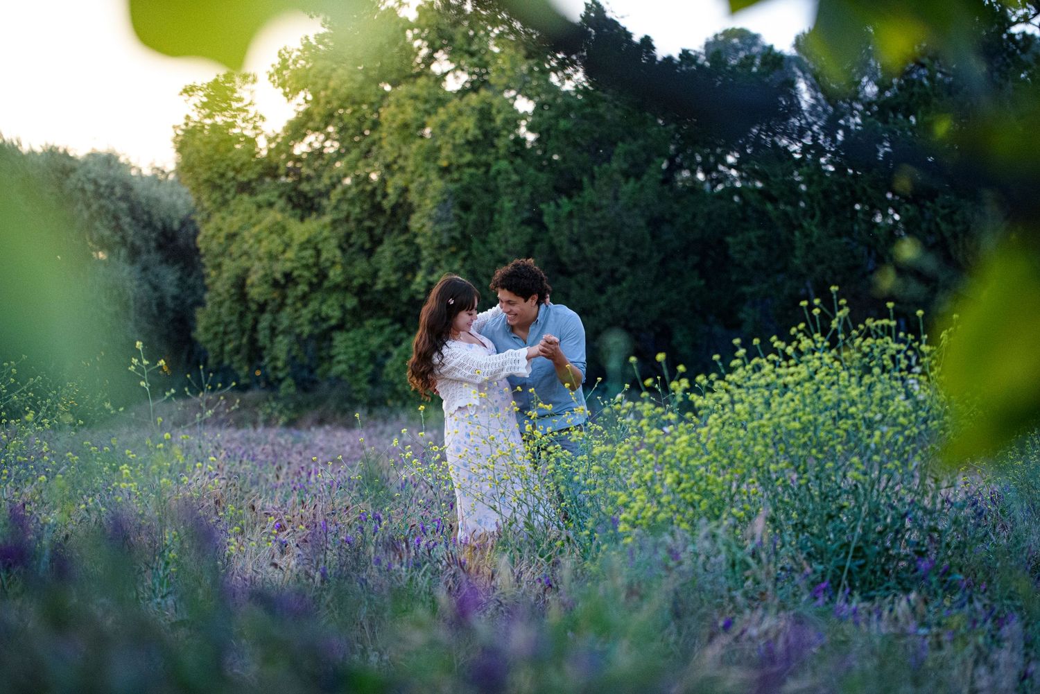 Couple dancing joyfully together in a vibrant lavender and wildflower field bathed in warm golden afternoon sunlight.
