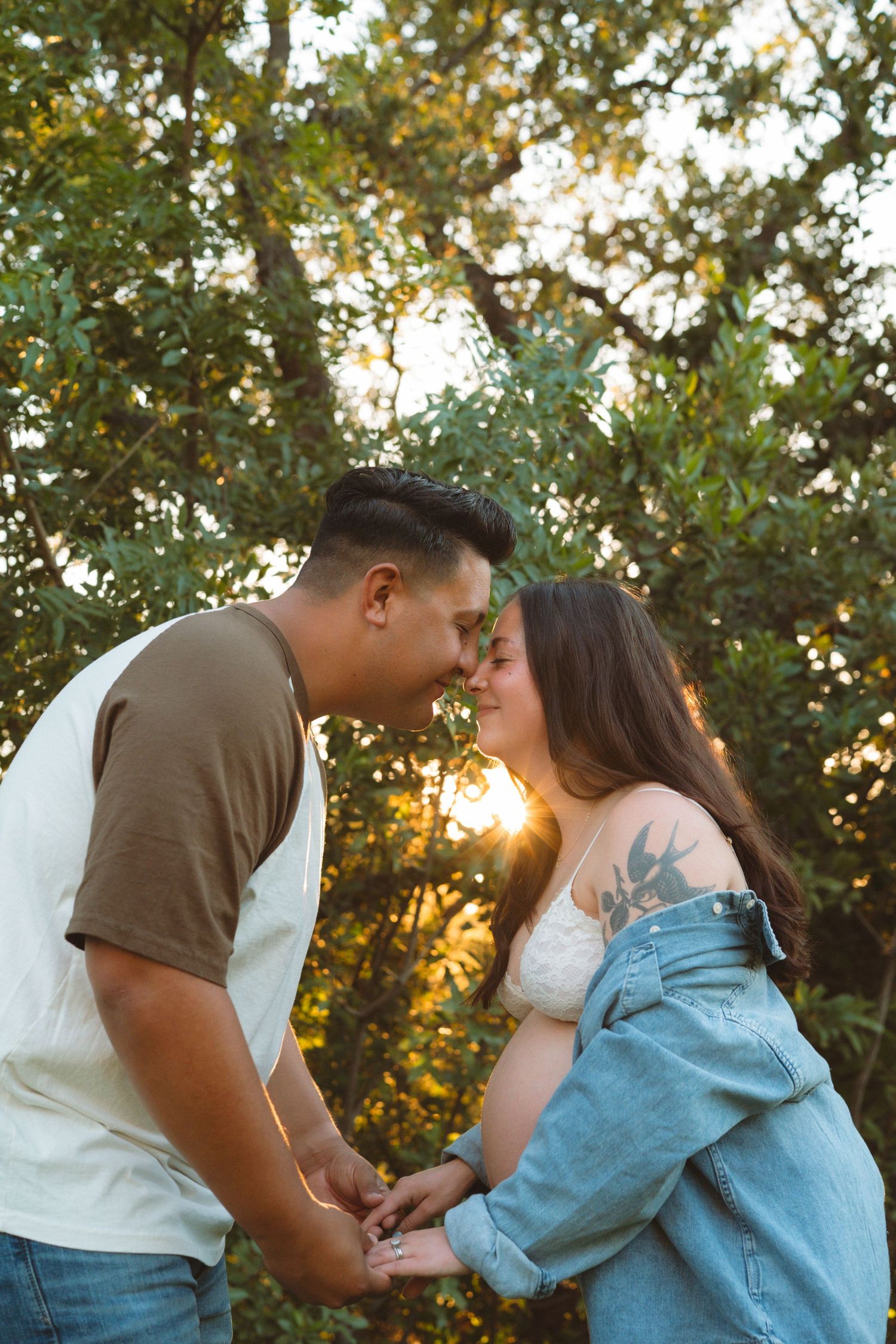 Couple sharing a tender moment nose-to-nose holding hands at sunset in a lush park.