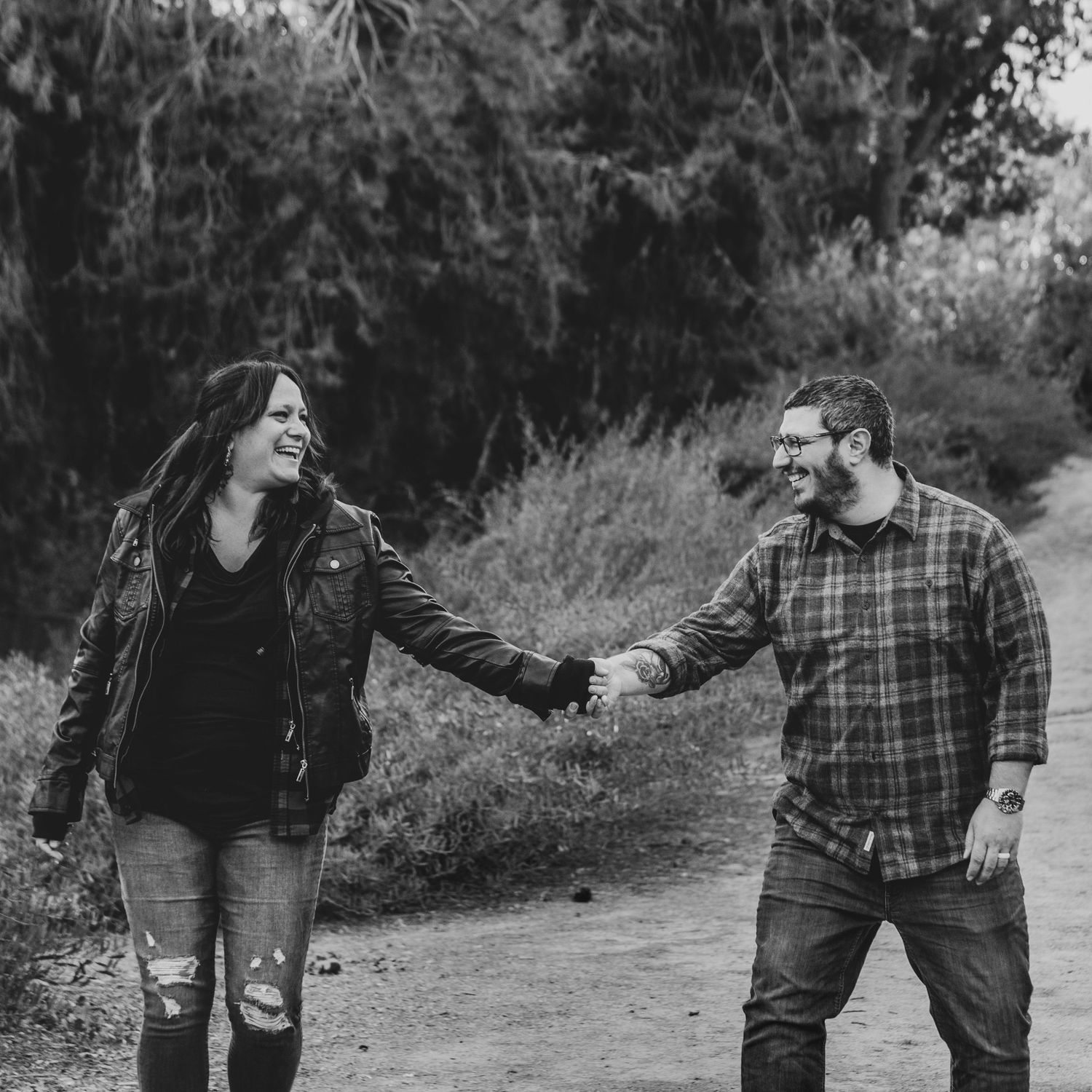 Joyful couple holding hands on a path in black and white photo.