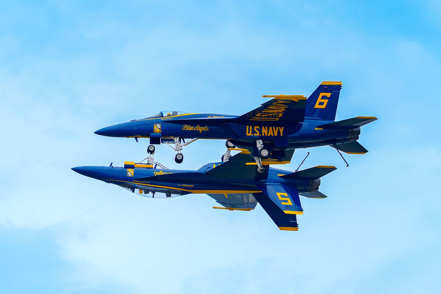 Two FA-18 Super Hornet fighter jets piloted by the Blue Angels are superimposed as one flies over the other.