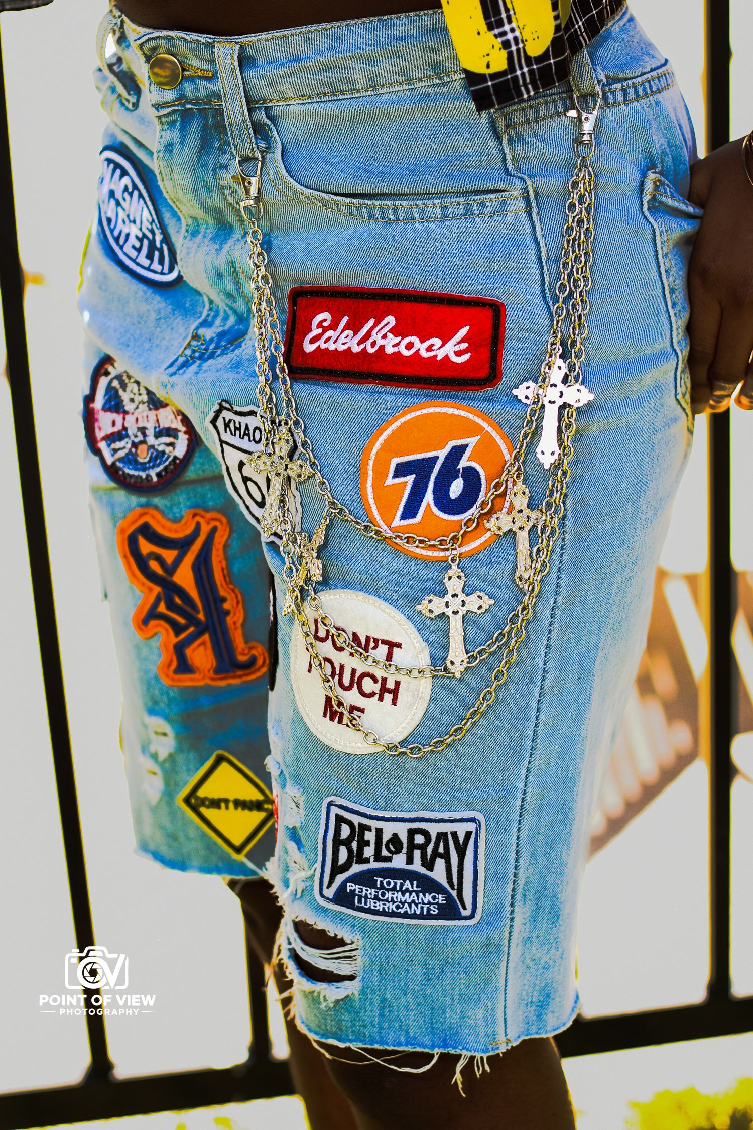 Close-up of denim shorts covered in colorful patches and cross chains by Point of View Photography.
