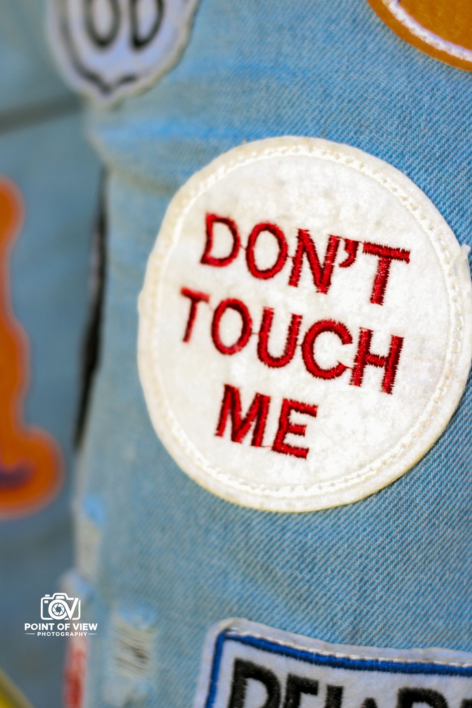 Embroidered patch on denim jacket reading DON'T TOUCH ME in red letters.