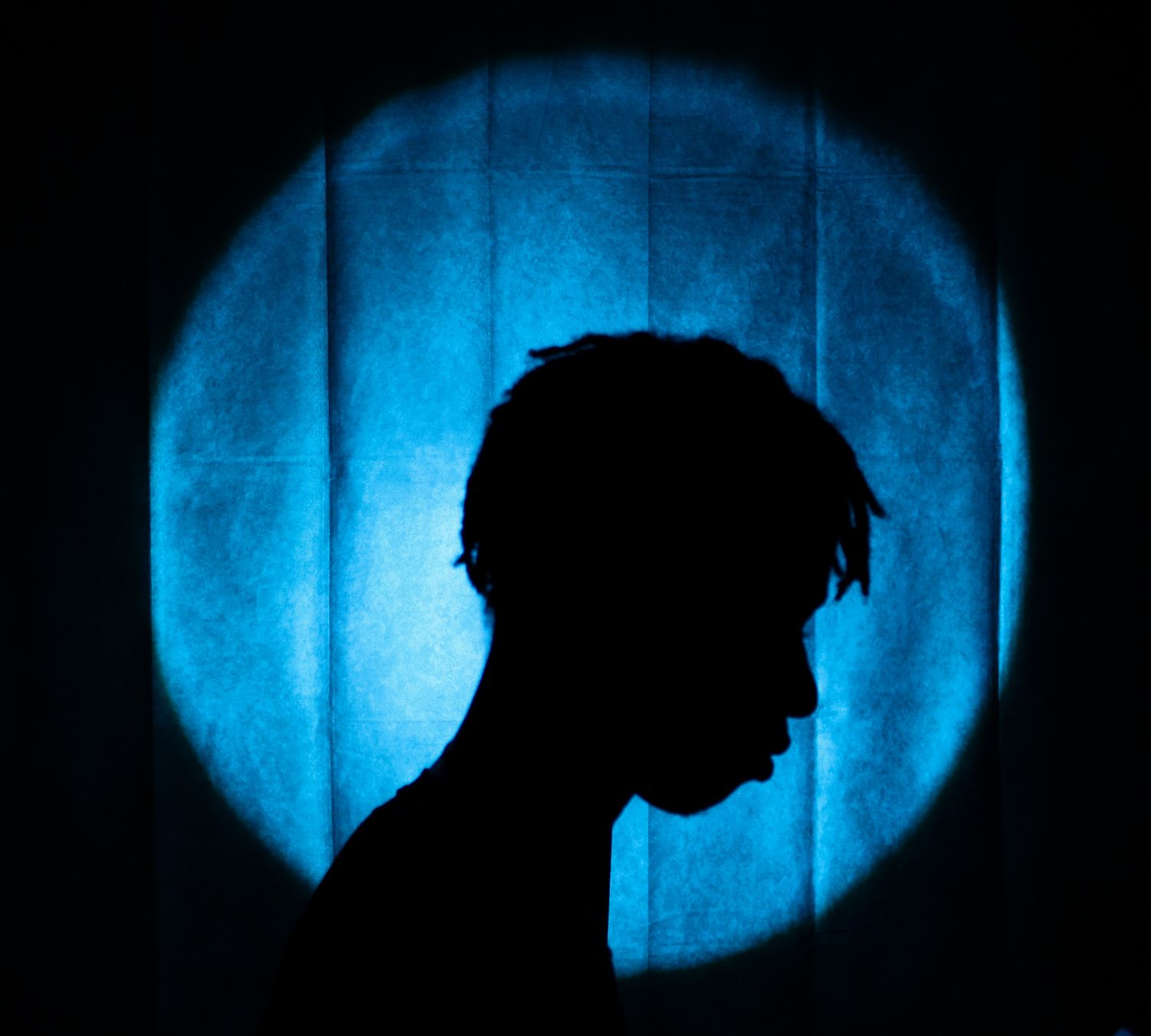 Artistic silhouette portrait of person with locs against glowing blue circular light background.
