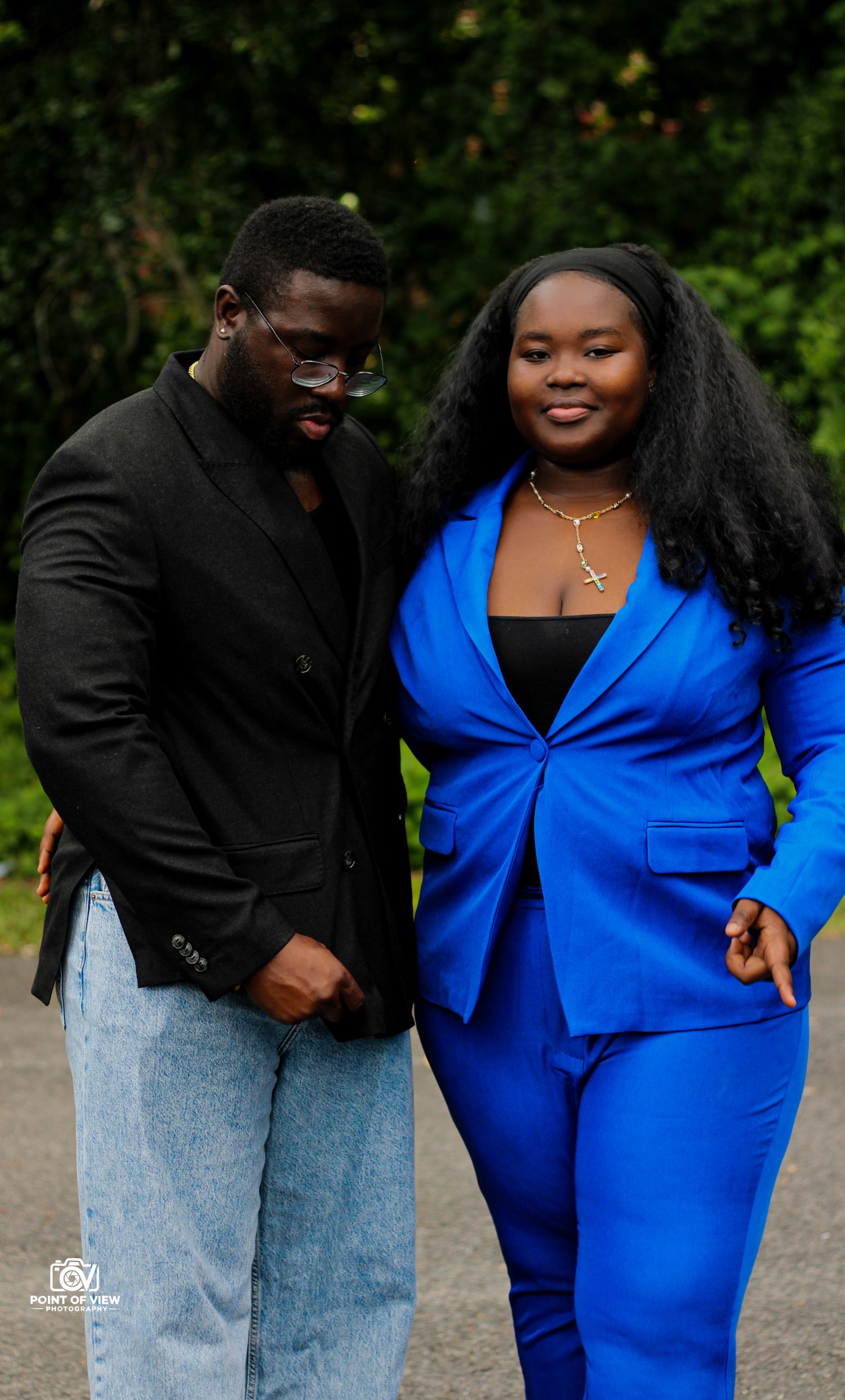 Smiling couple walking outdoors, man in black blazer, woman in vibrant royal blue suit.