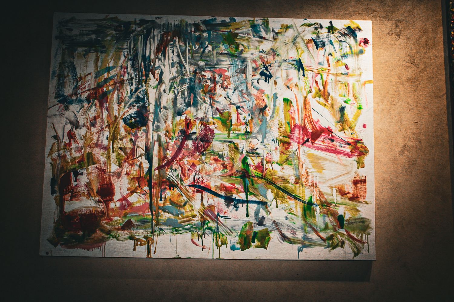 A vibrant abstract expressionist painting with colorful brushstrokes displayed on a wall in dim lighting.
