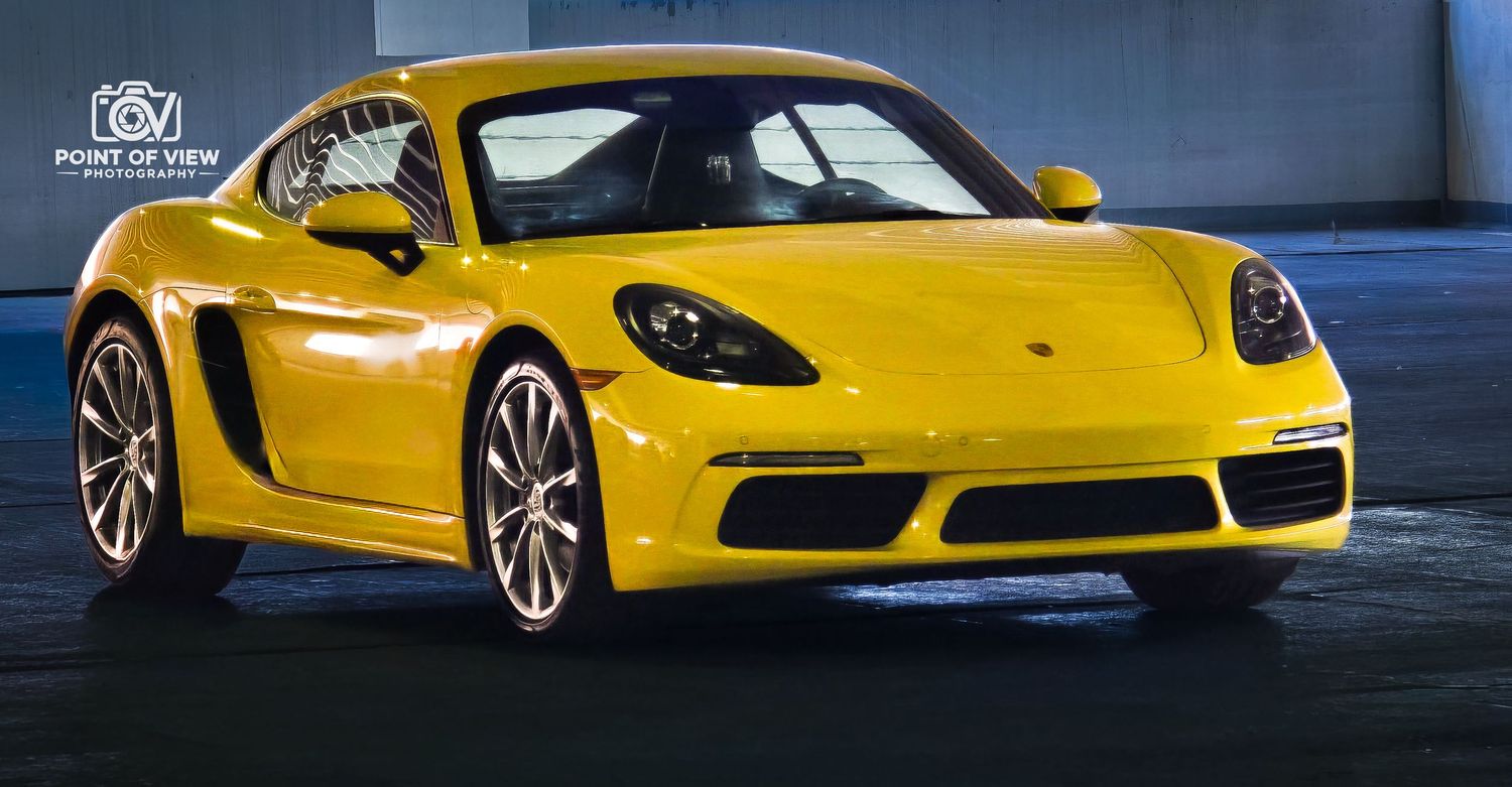 A bright yellow Porsche 718 Cayman sports car parked in an urban setting with dramatic lighting.