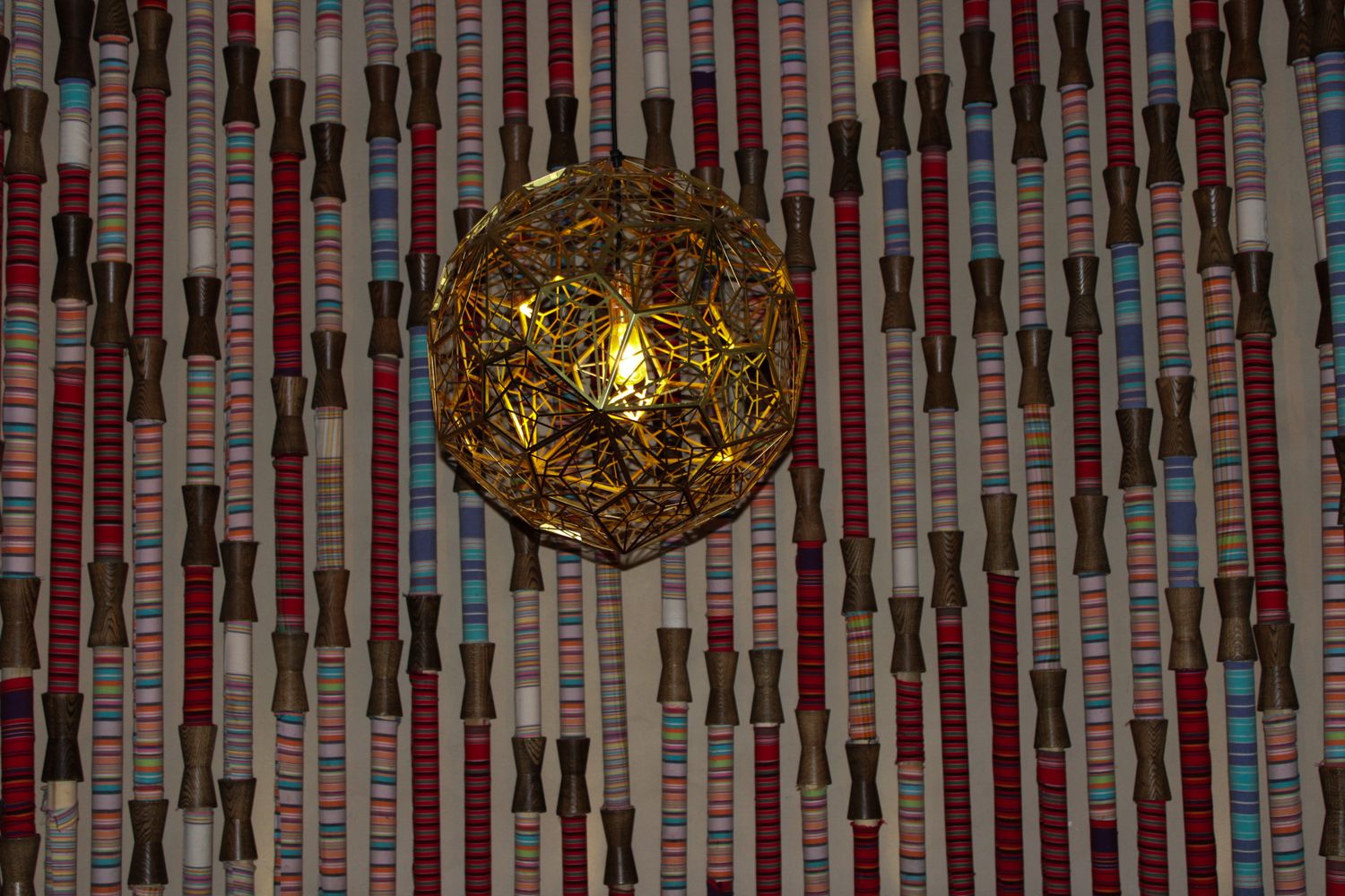 A decorative gold geometric pendant light hangs against a colorful striped patterned ceiling.