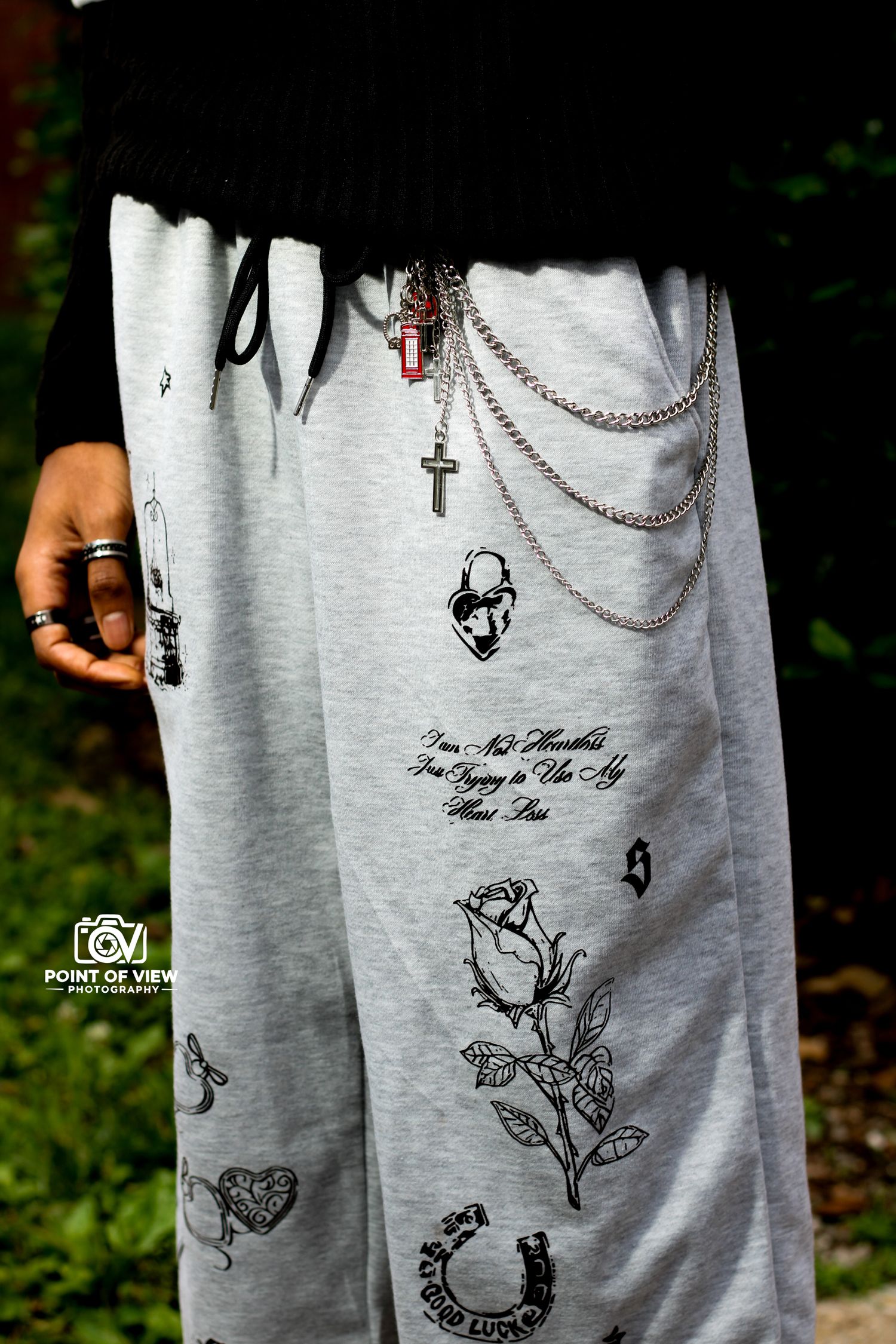Detailed view of gray printed sweatpants featuring rose graphics and layered cross chain accessories.