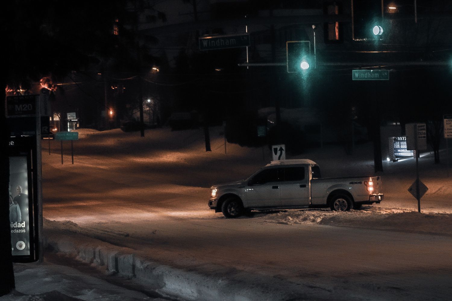 Silver pickup truck at snowy intersection at night with green traffic light.