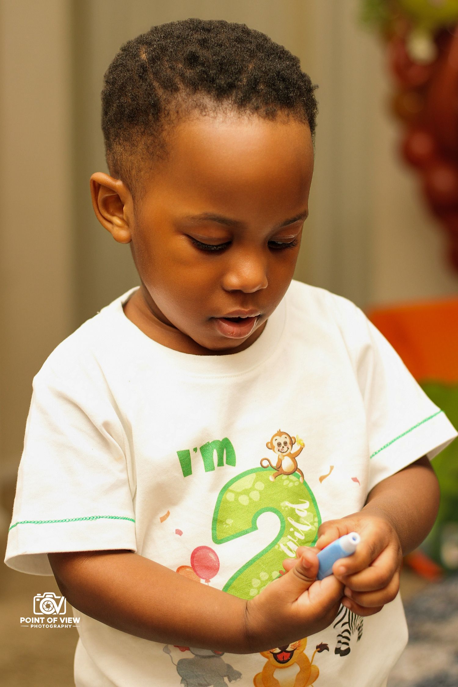 Adorable toddler in white birthday shirt celebrating turning 2 years old at party.